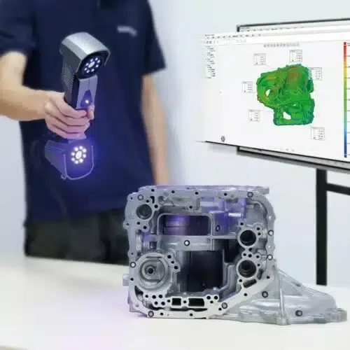 Une personne utilisant un scanner 3D pour inspecter un composant mécanique complexe placé sur une table, avec un moniteur à côté affichant un modèle numérique en couleur.