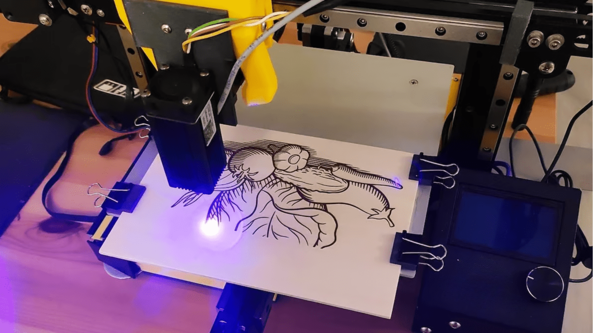 Une imprimante 3D en action imprimant une illustration détaillée d'une plante avec un visage, utilisant une lumière bleue UV pour révéler l'encre sur une planche en bois.