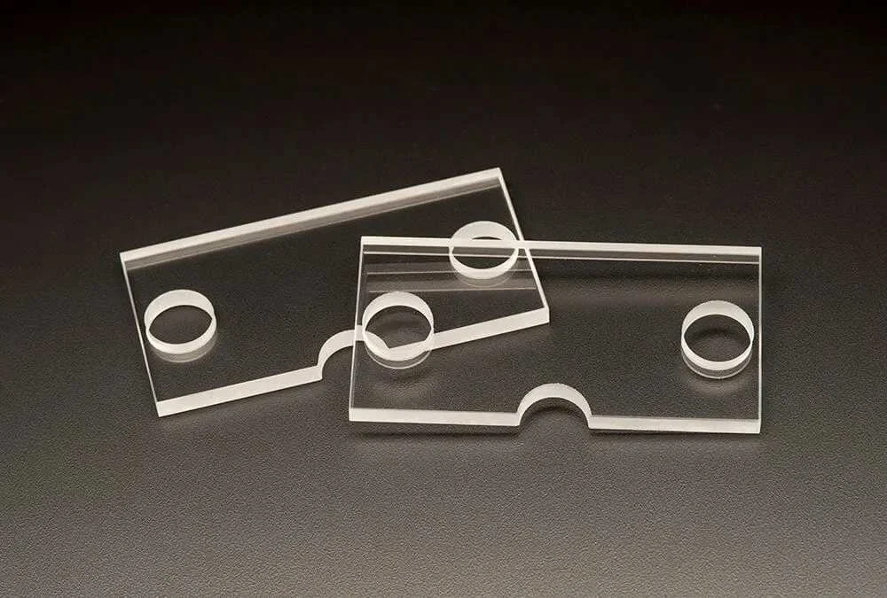 Deux plaques de verre rectangulaires transparentes avec des trous ronds en haut à gauche et au centre, posées sur une surface noire.