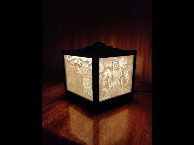 Lampe de chevet avec des images en noir et blanc sur ses côtés, éclairée dans une pièce sombre.