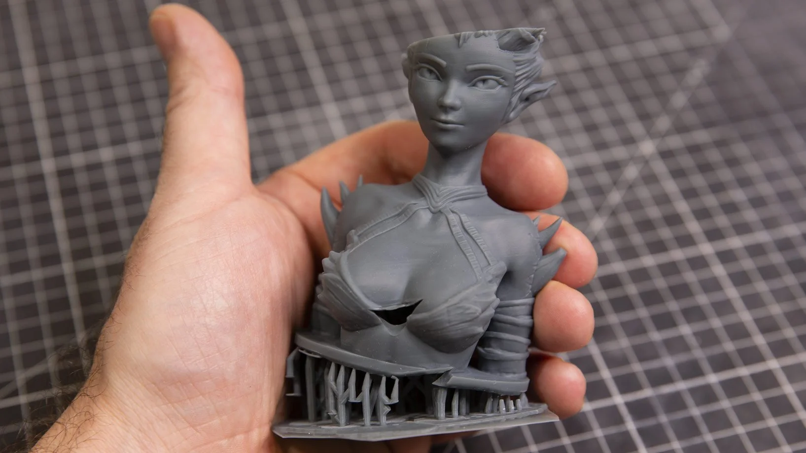 Figura de figurine en gris représentant une femme aux traits elfiques, avec une peau très détaillée et une base en forme de structure complexe.