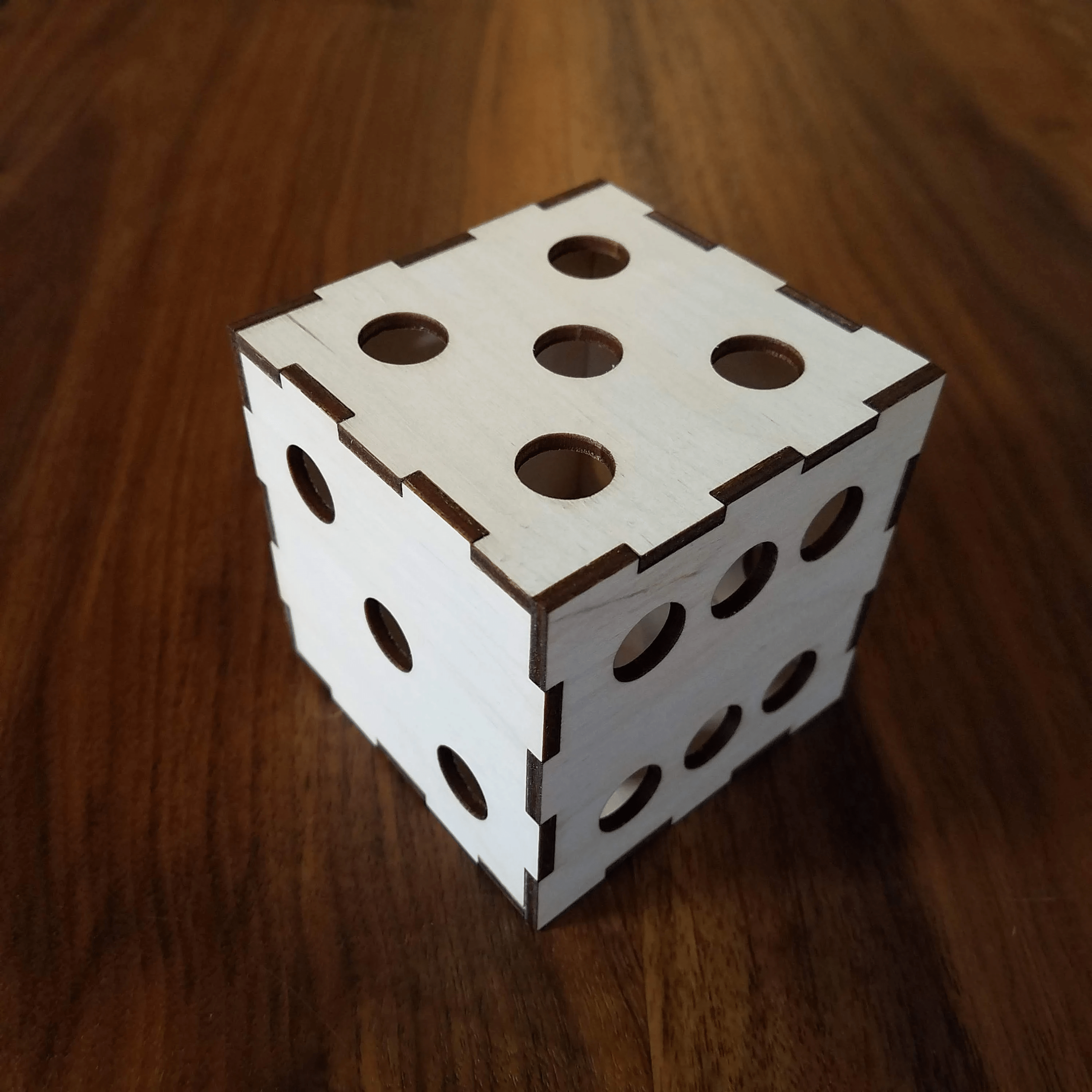 Cube en bois avec des trous ronds, assemblé à partir de pièces en bois. Le cube est posé sur une surface en bois.