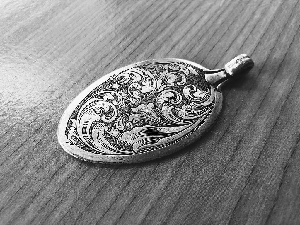 Médaillon en argent orné d'ornements floraux gravés, posé sur une surface en bois.