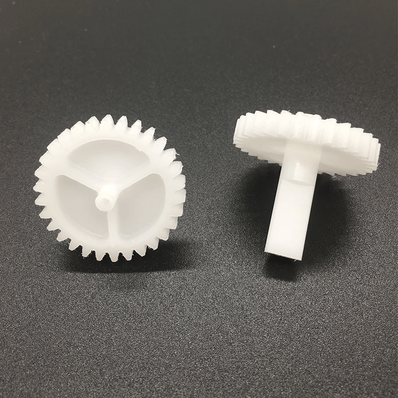 Deux engrenages en plastique blanc, un à côté de l'autre, reposant sur une surface noire.