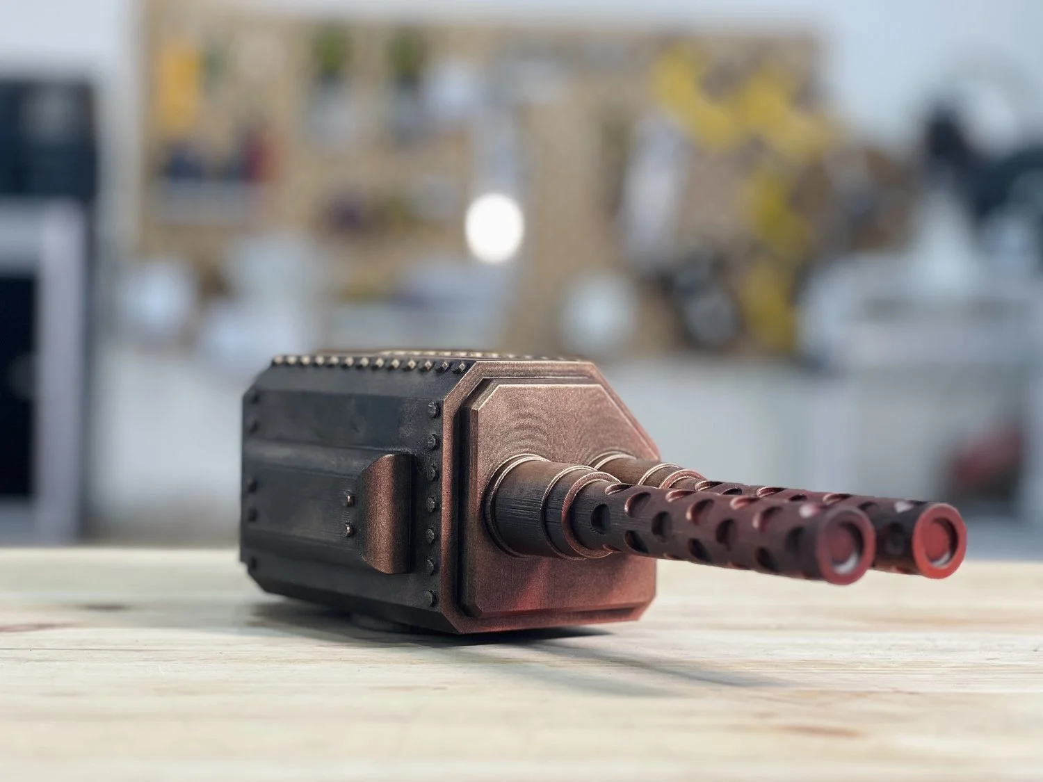 Une maquette de canon sci-fi en forme de cube, avec deux tubes de canon rouge foncé, sur une surface en bois, avec un fond flou contenant des objets colorés.