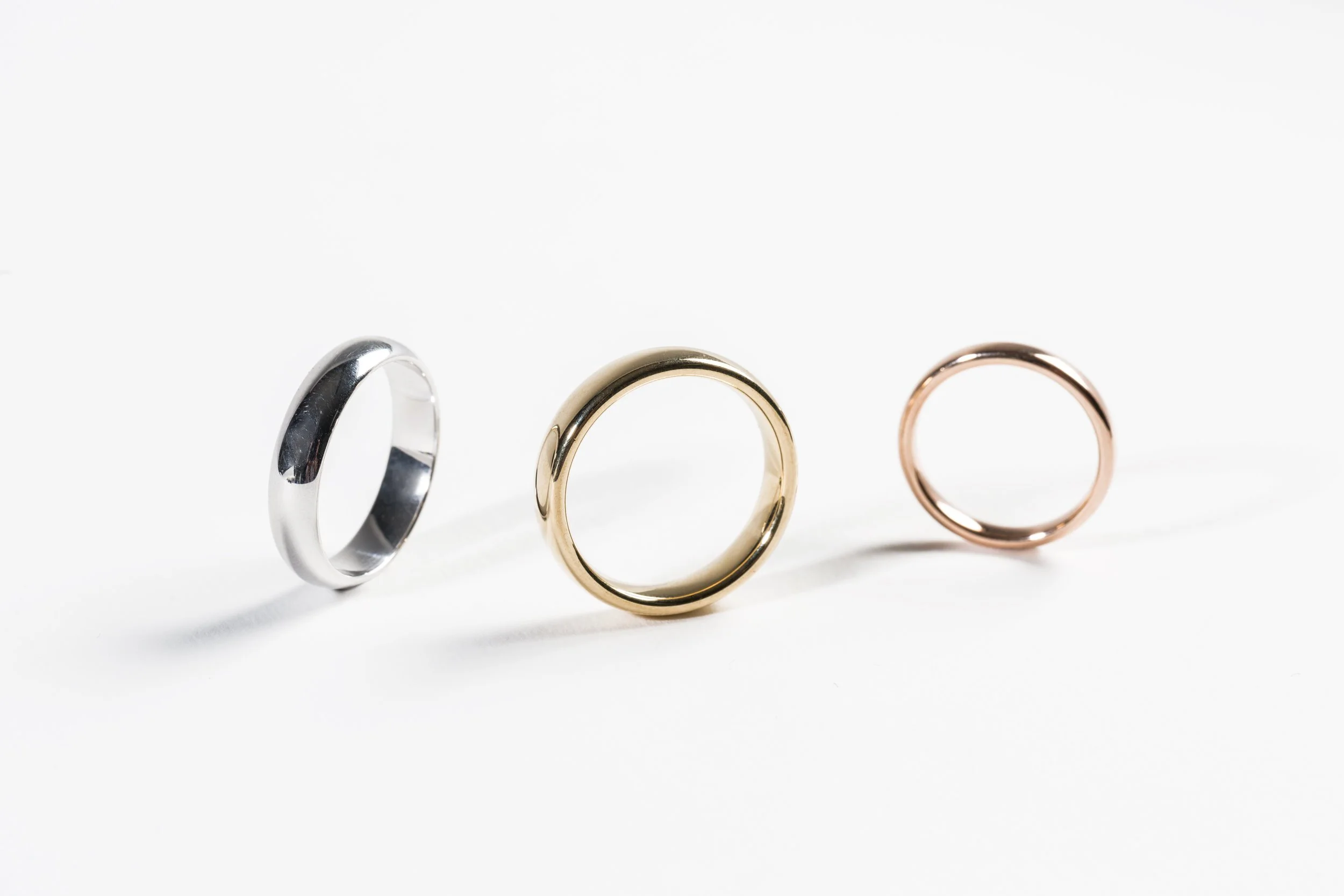 Trois anneaux en métal de différentes couleurs (argent, or, rose), alignés sur une surface blanche.