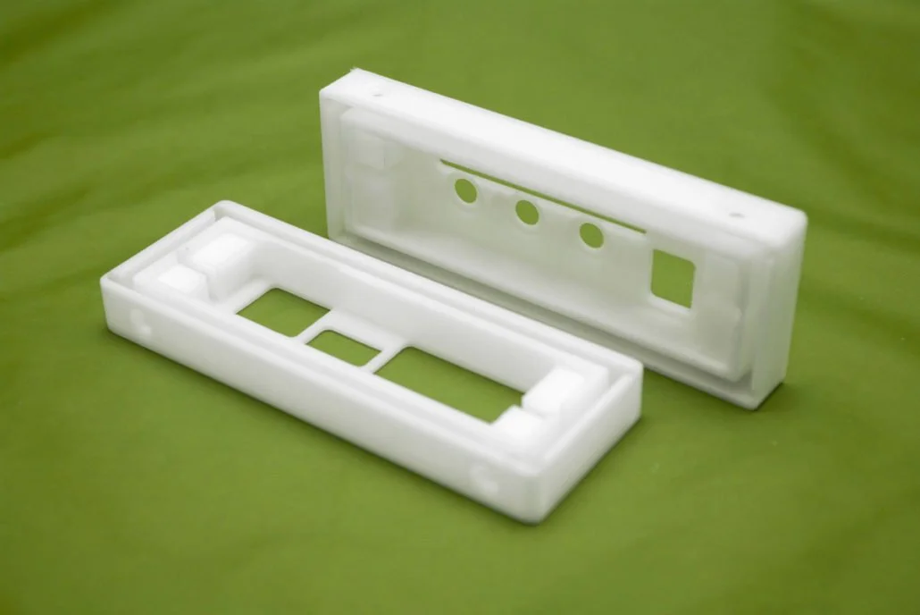 Deux boîtiers en plastique blanc pour appareils électroniques, posés sur une surface verte.