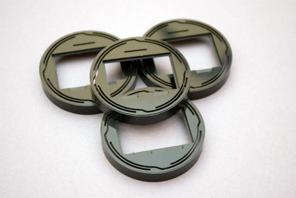 Quatre cadres de montre en plastique noir avec des fenêtres rectangulaires, disposés sur une surface blanche.