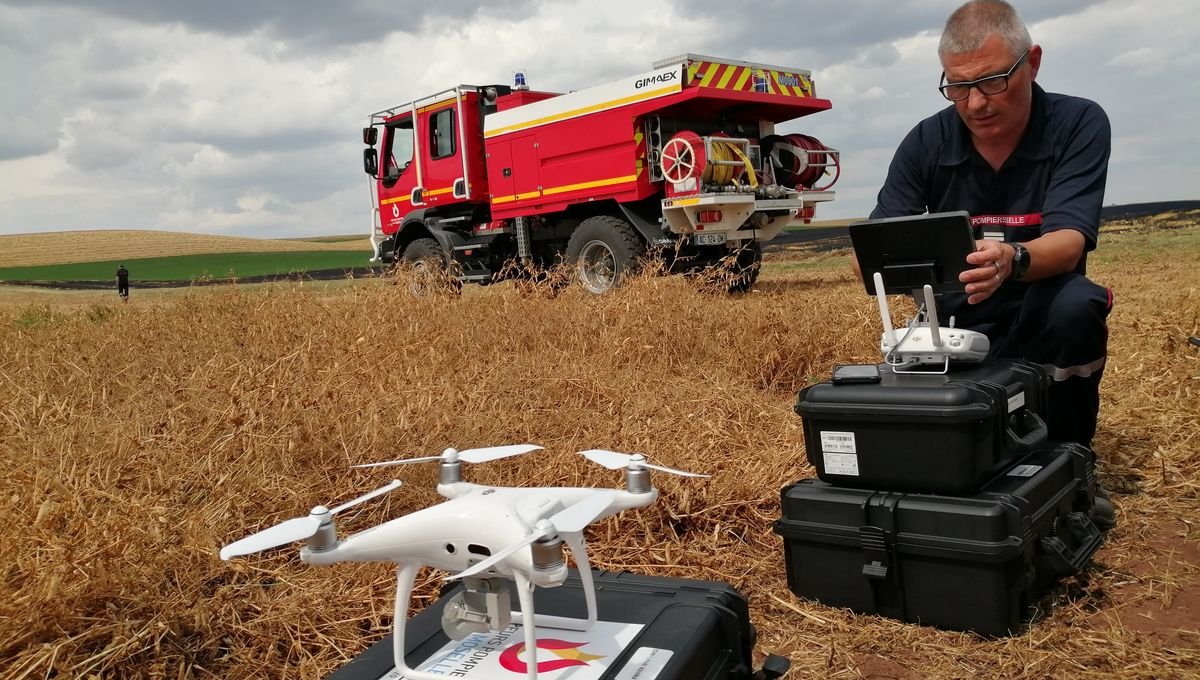 Pompier utilisant un drone dans un champ avec un véhicule de secours en arrière-plan