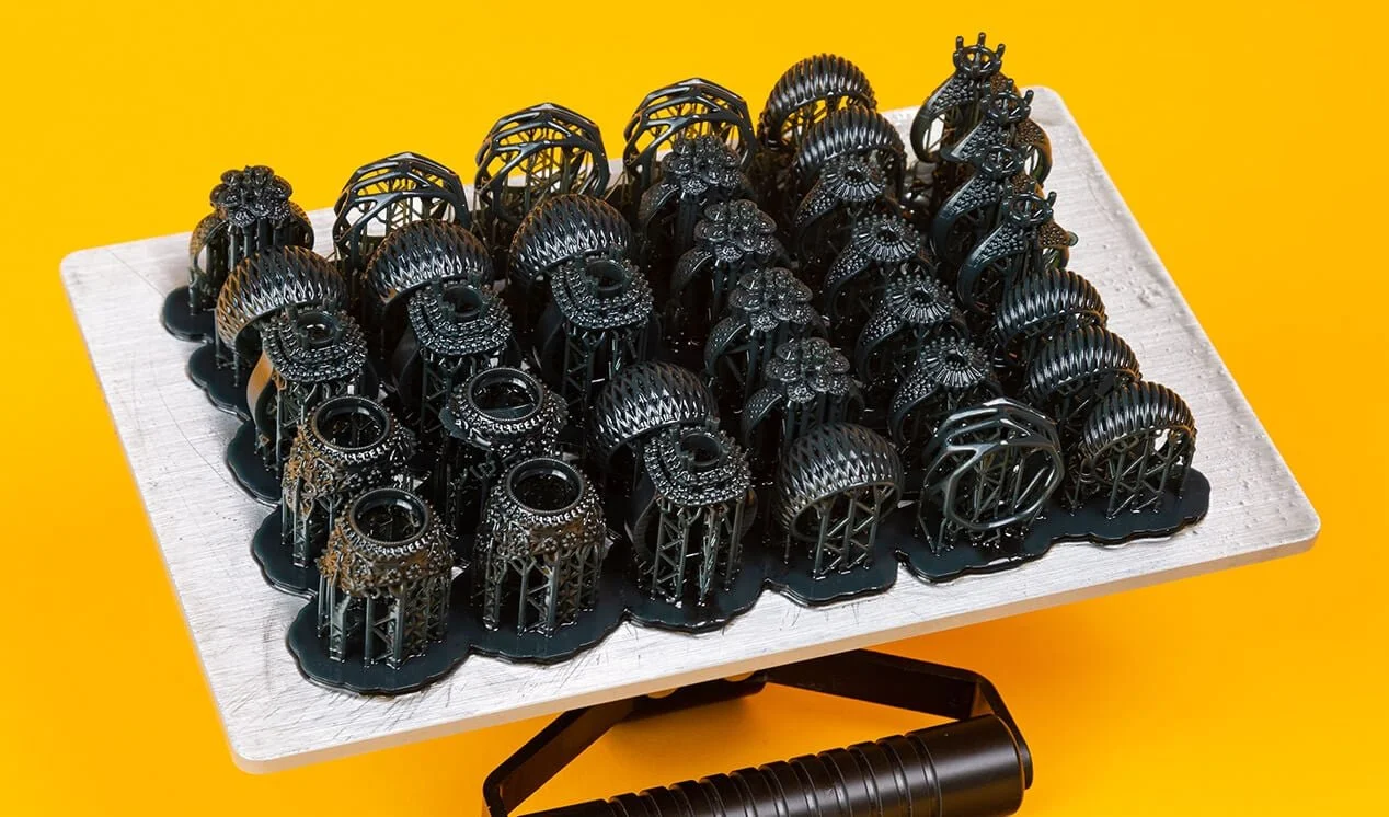 Une collection de bagues en métal noir posées sur une plaque blanche, avec un fond jaune.