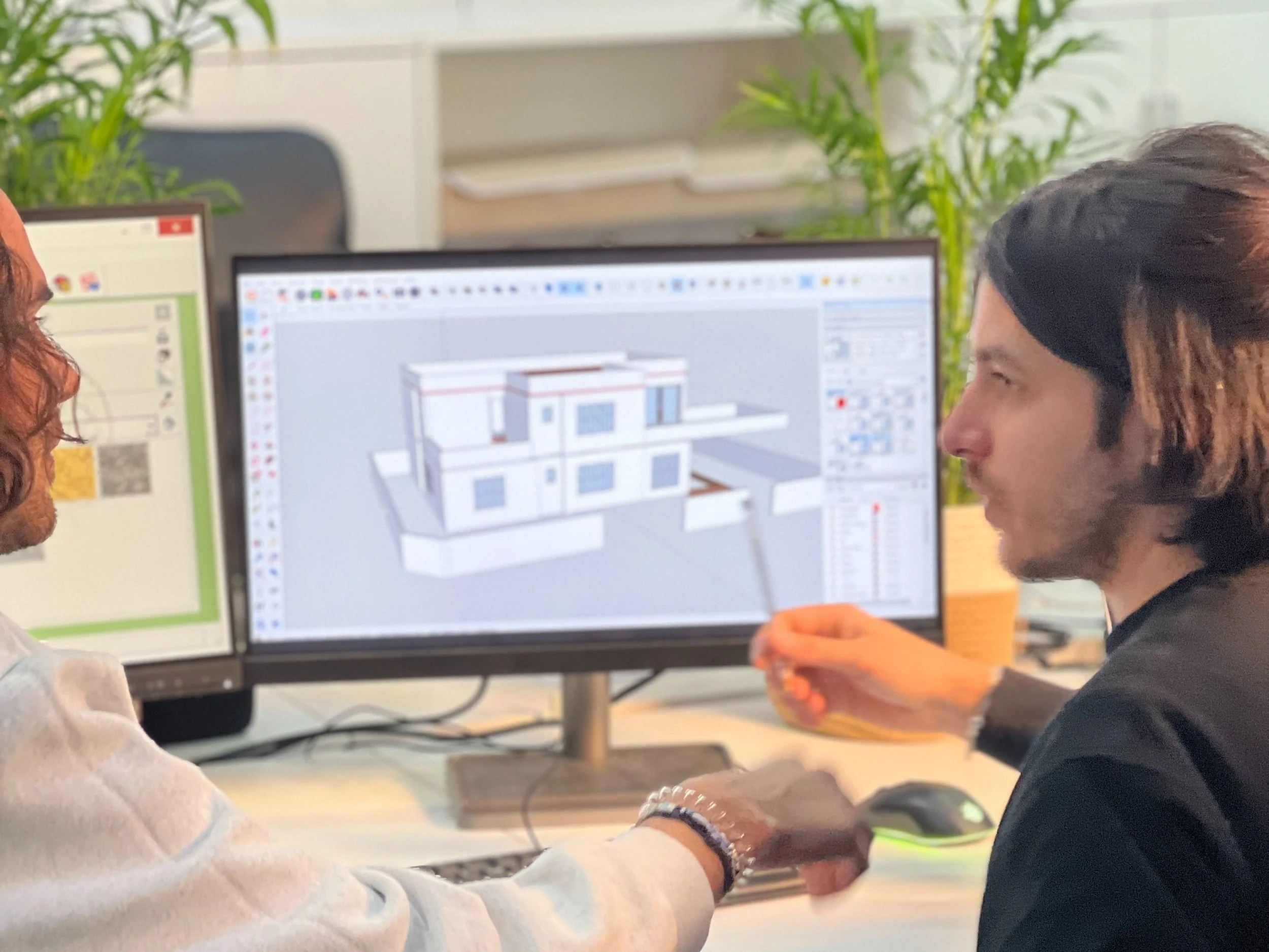 Deux personnes discutent devant un ordinateur qui affiche un modèle 3D d'un bâtiment.