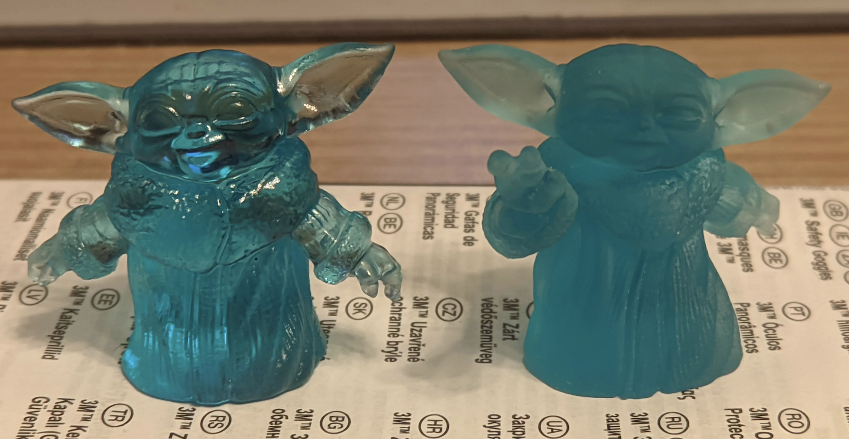 Deux figurines de Baby Yoda en plastique coloré, posées sur un papier avec du texte