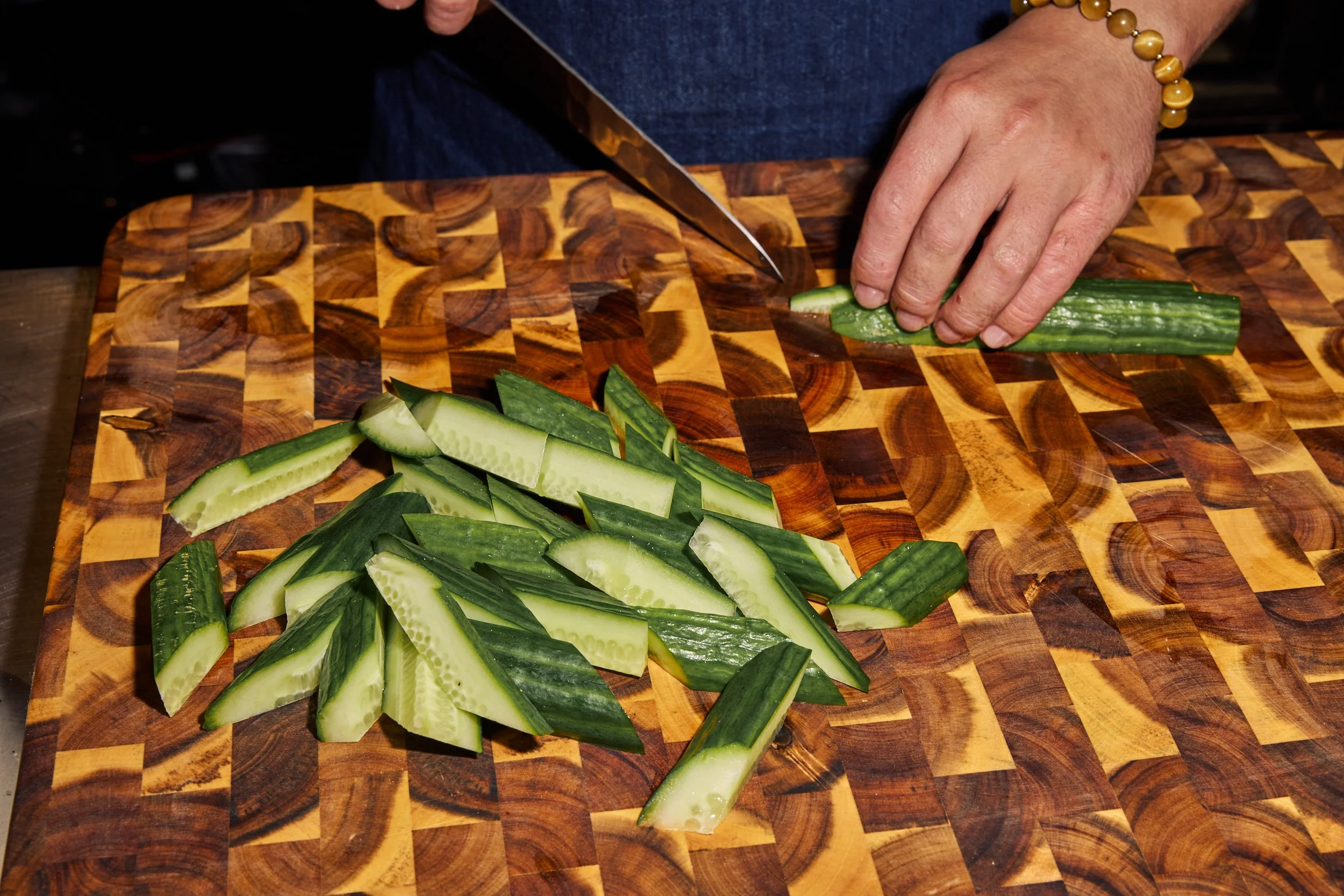 Chef slicing locally-sourced cucumbers on a wooden cutting board.