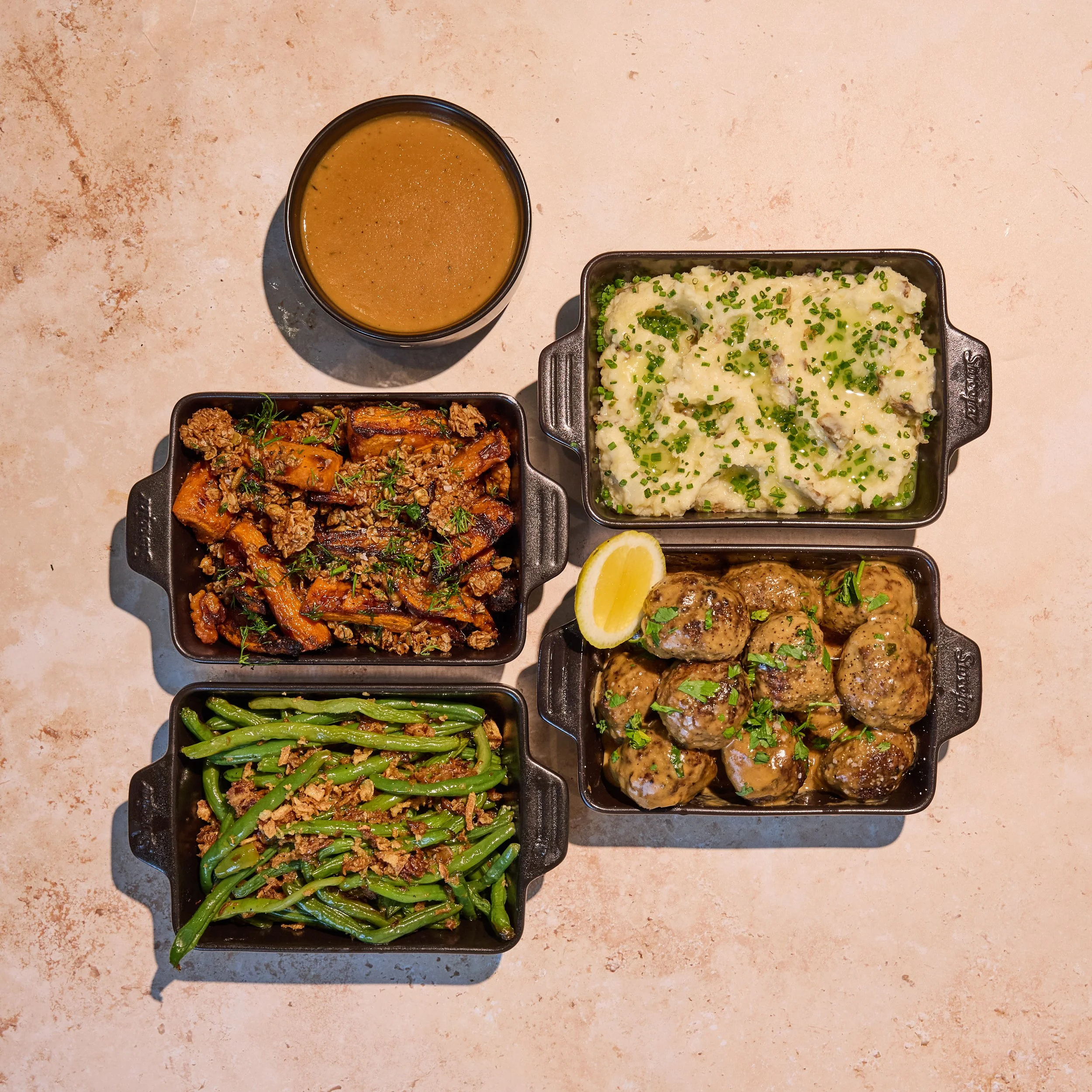 Meatballs & Mash Family Meal. Overhead view of a hearty meal with gravy, mashed potatoes, roasted carrots, meatballs, and green beans in serving dishes.