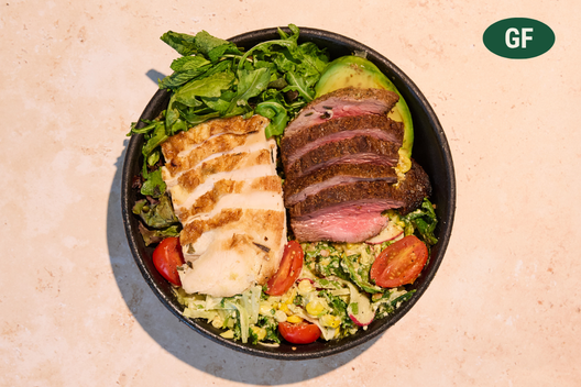 Skinny protein plate with sliced grass-fed steak, rosemary roasted chicken breast, charred corn salad, half avocado, and farm greens with mint.