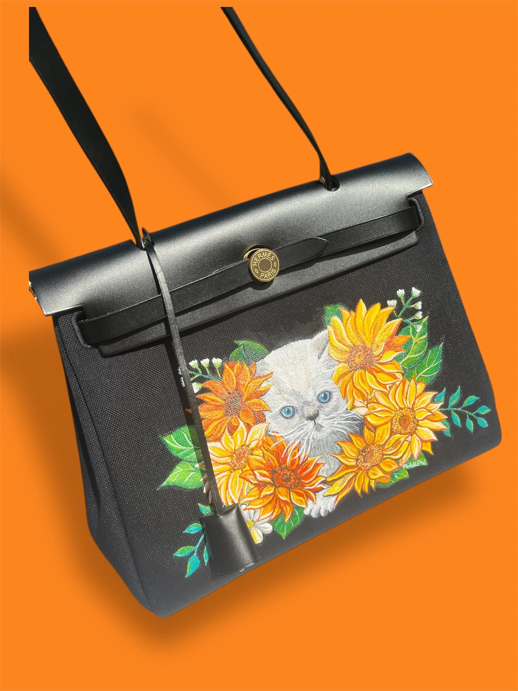 The family's baby kitten surrounded by orange and yellow sunflowers hand painted on her Hermes Her bag. 