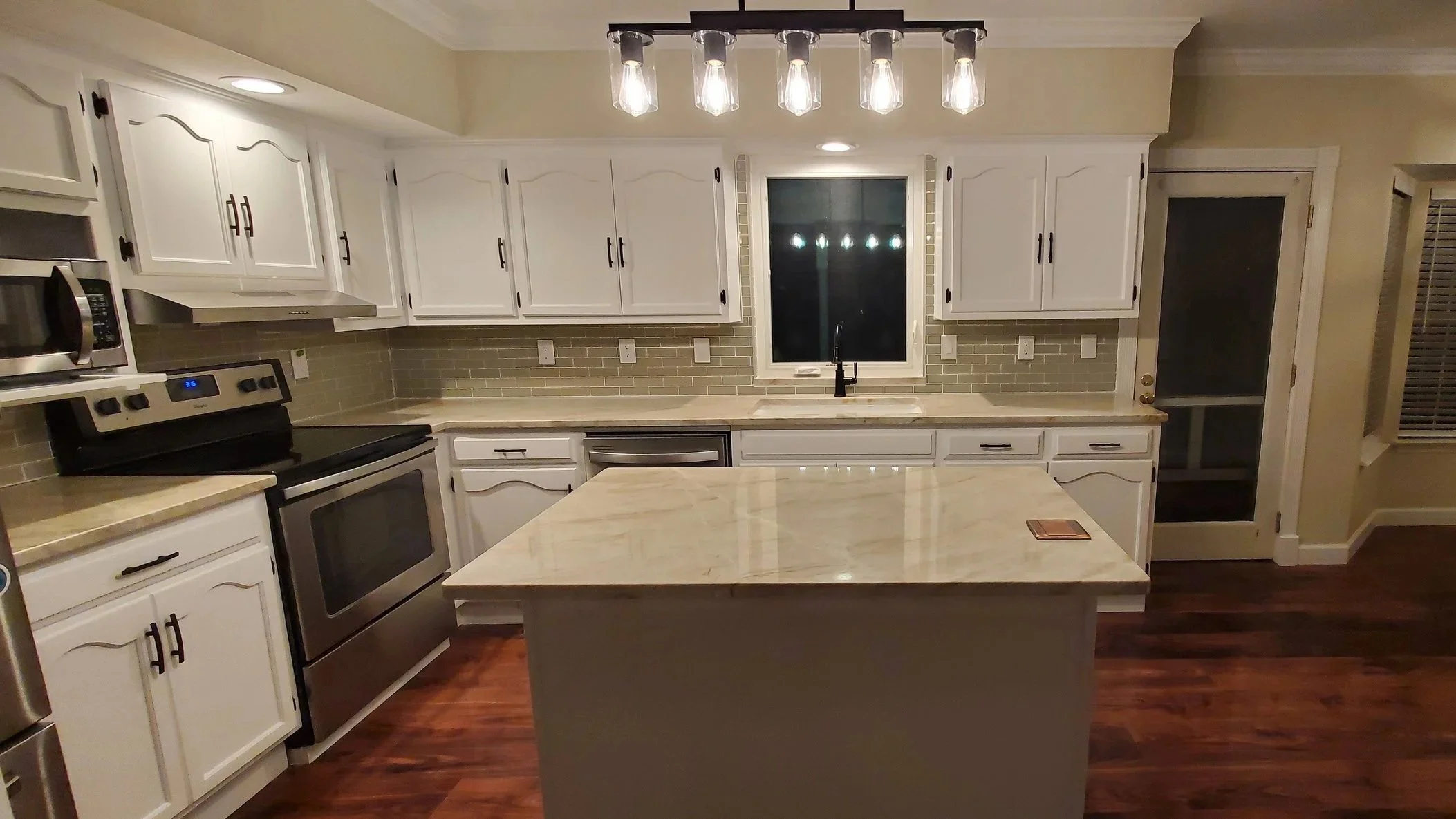 Kitchen renovation in Cleveland, TN showing custom island with popup outlet, new counters and backsplash, refinished cabinets, LVP floor