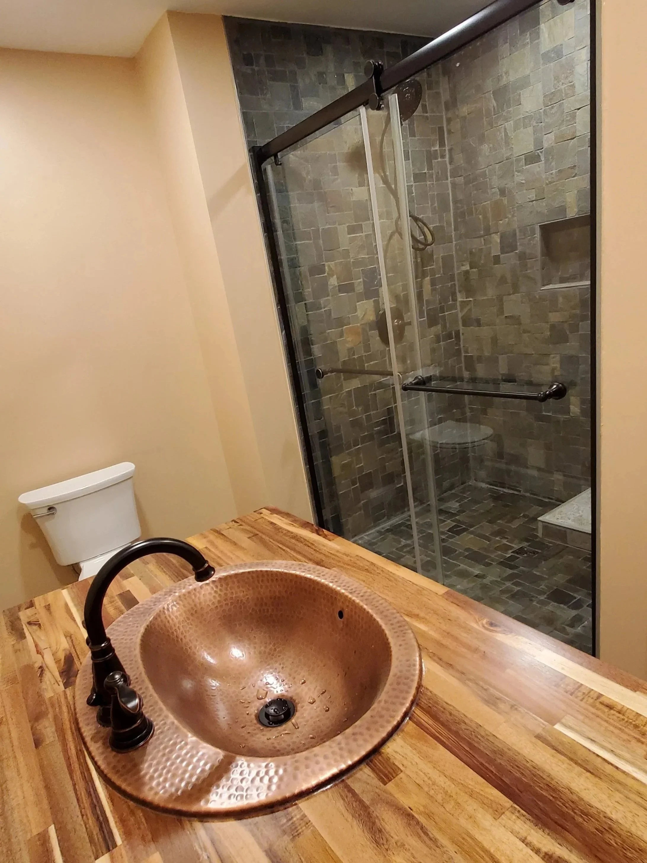 Basement bathroom addition in East TN, showing tile shower with floating bench, butcher block countertop, hammered copper sink