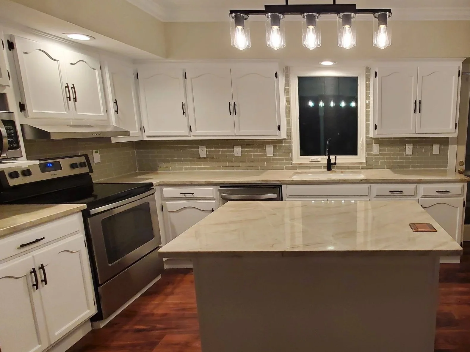 Kitchen renovation in Cleveland,, TN showing custom island with popup outlet, new counters and backsplash, refinished cabinets, LVP floor