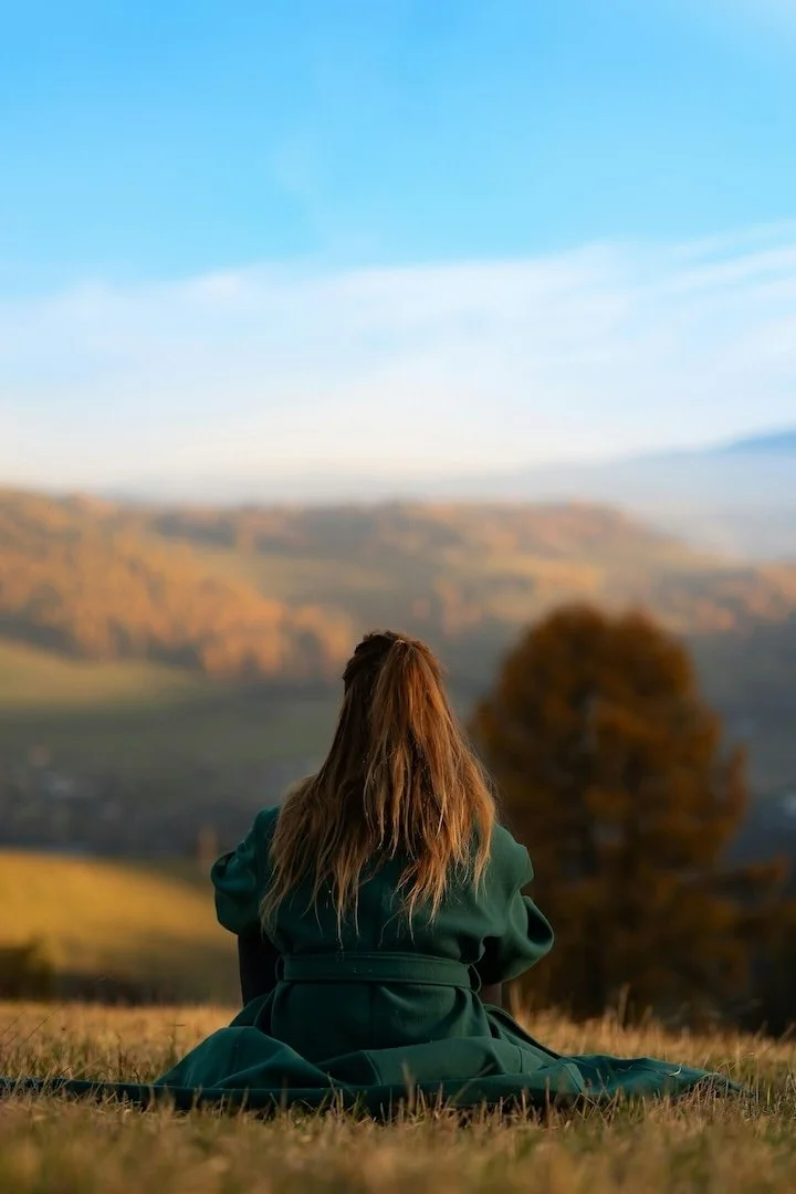 woman sits on a blanket, looking away from the camera, mountain view in the distance, are therapy intensives worth it? EMDR therapy intensives near Boston and NYC