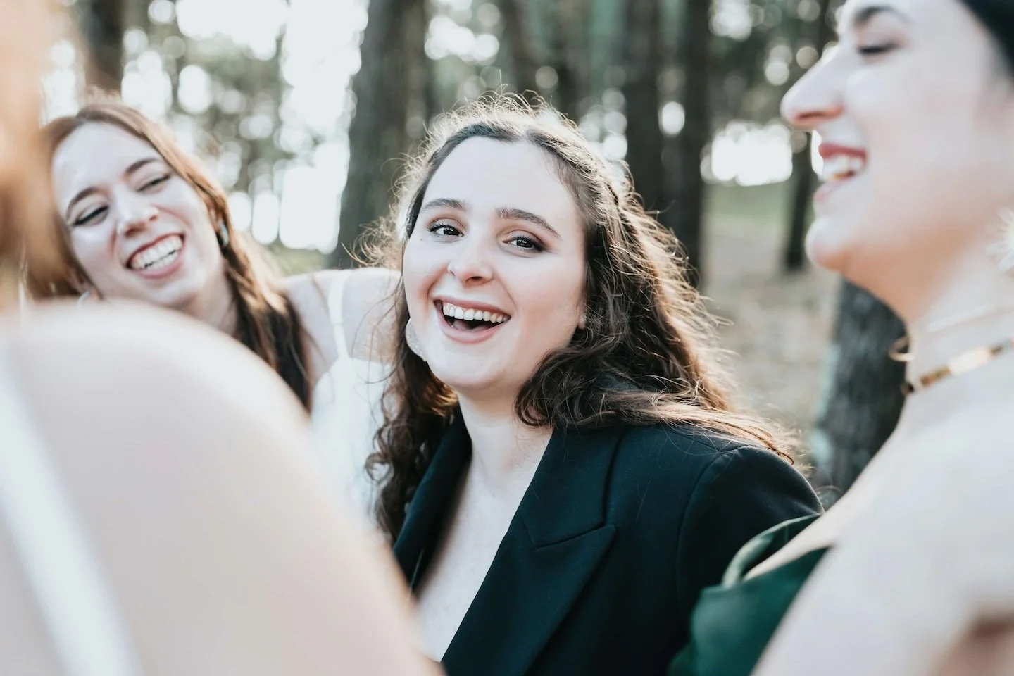Four women smiling and laughing together in an outdoor forest setting, close-up group portrait. EMDR therapy and EMDR intensives for women, LGBTQ+ in Massachusetts, online EMDR in Boston, MA