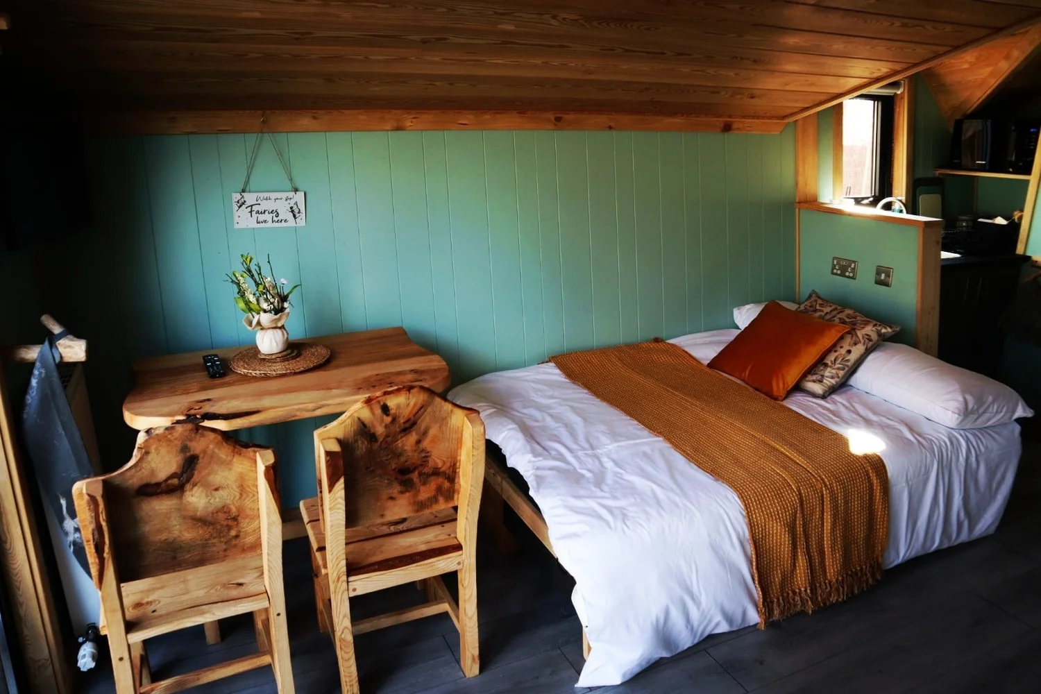 Witches Cabin interior with a double bed, sage walls and rustic wooden dining furniture