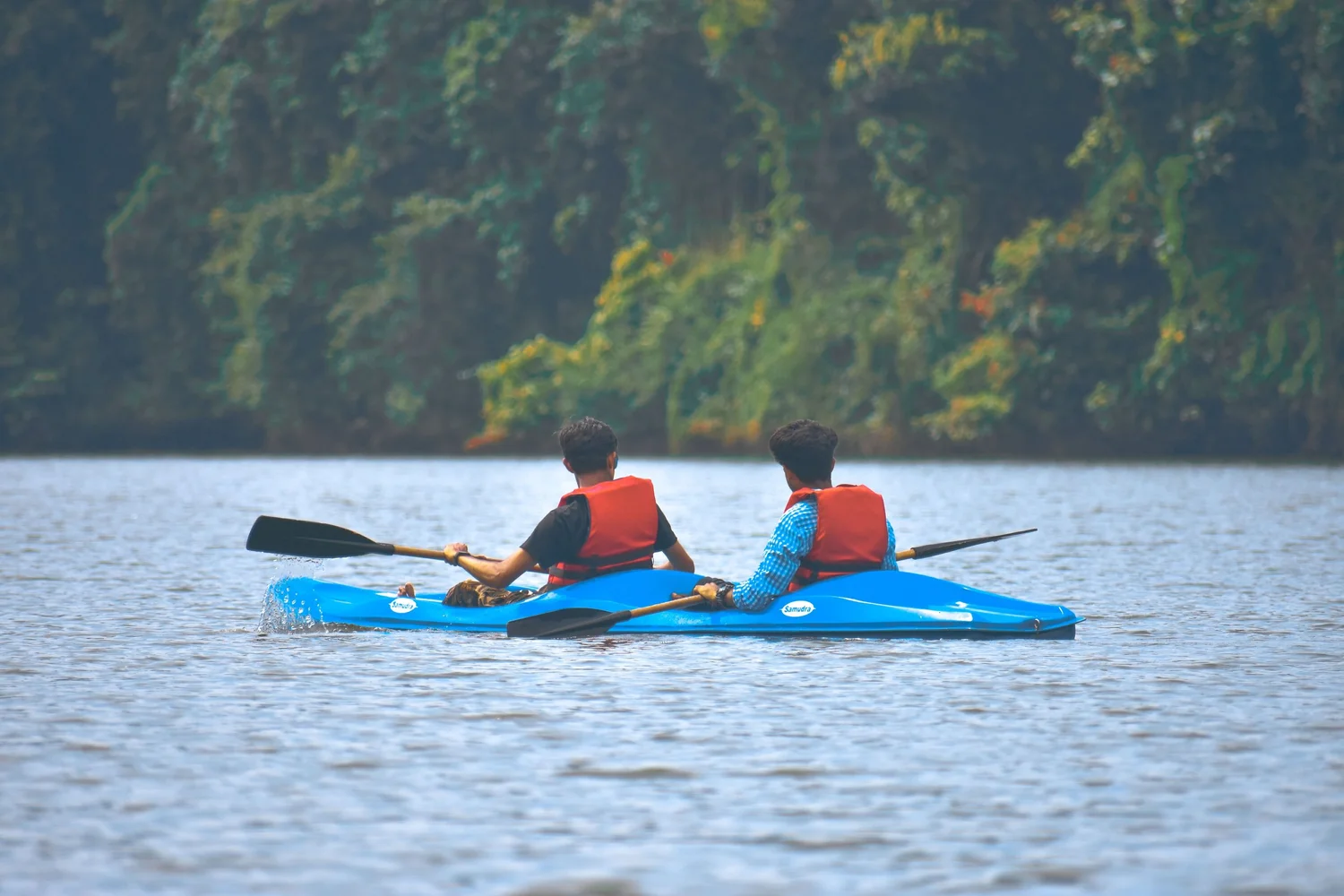 Two people kayaking on calm water wearing buoyancy aids