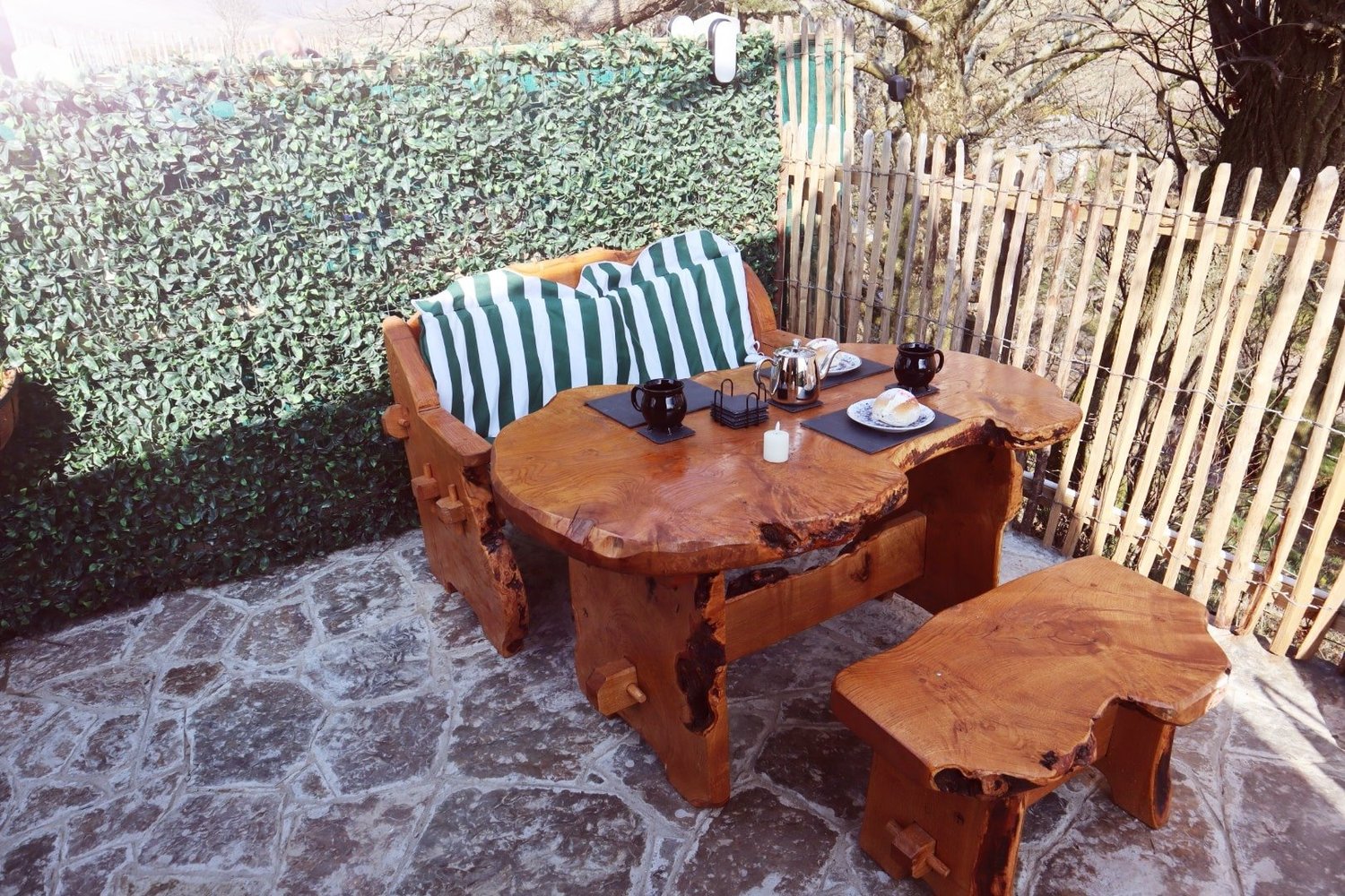 Private stone patio with a rustic wooden table and outdoor seating with striped cushions