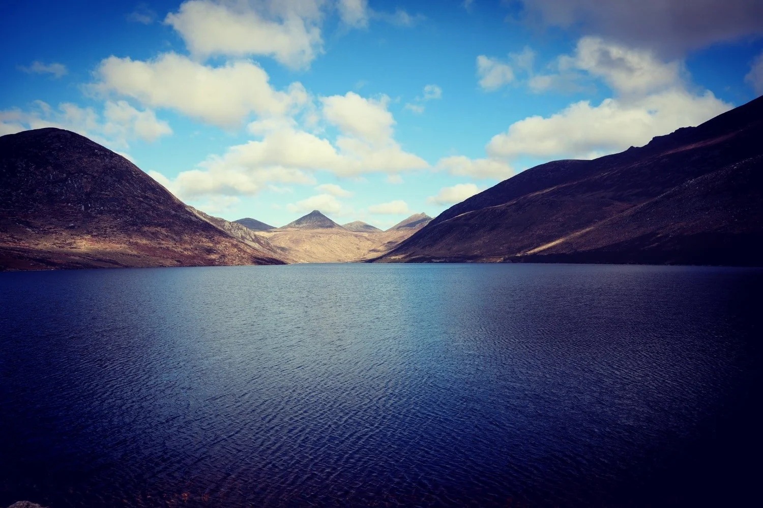 Reservoir water framed by the Mourne Mountains beneath a blue, cloud-filled sky