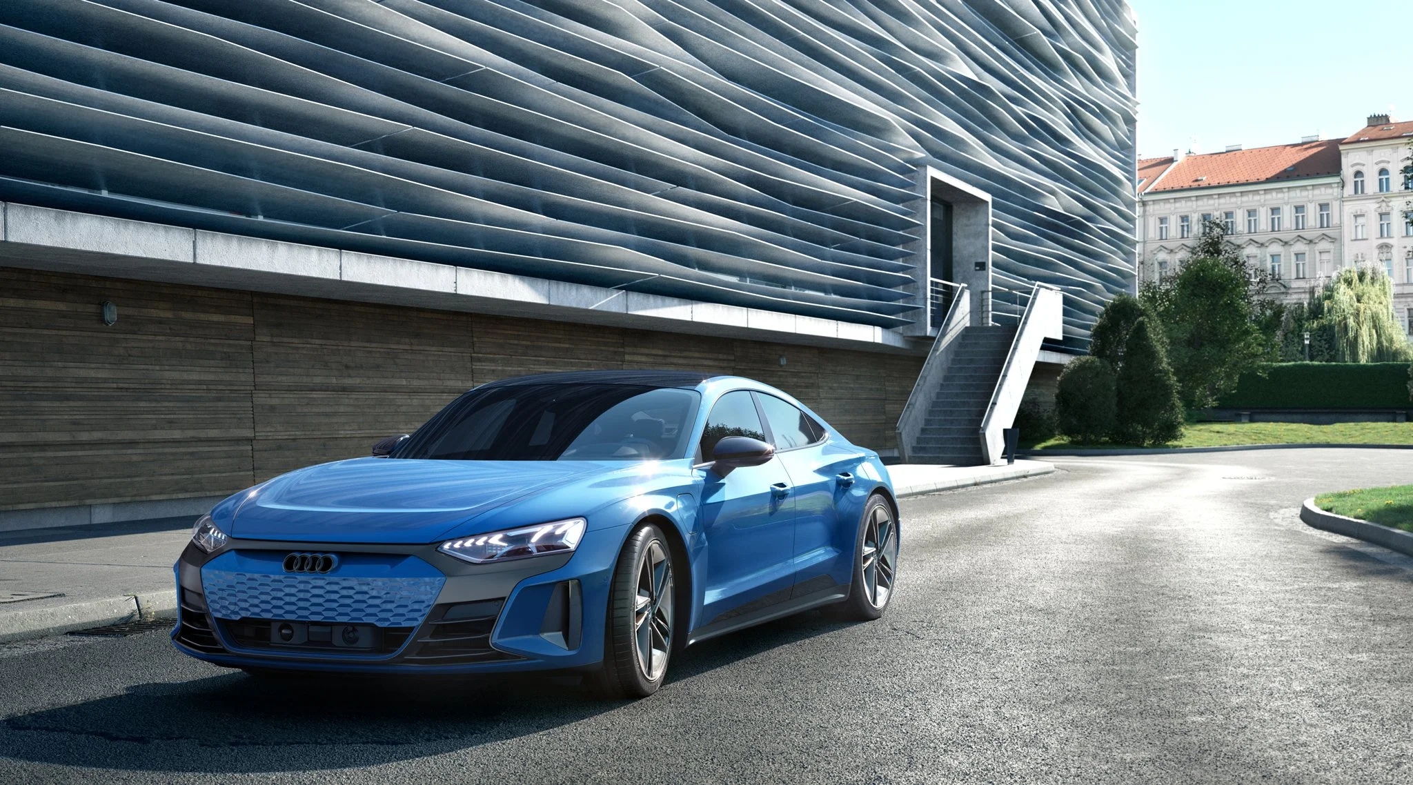 Blue Audi sedan parked on street near modern building and greenery in an urban setting.