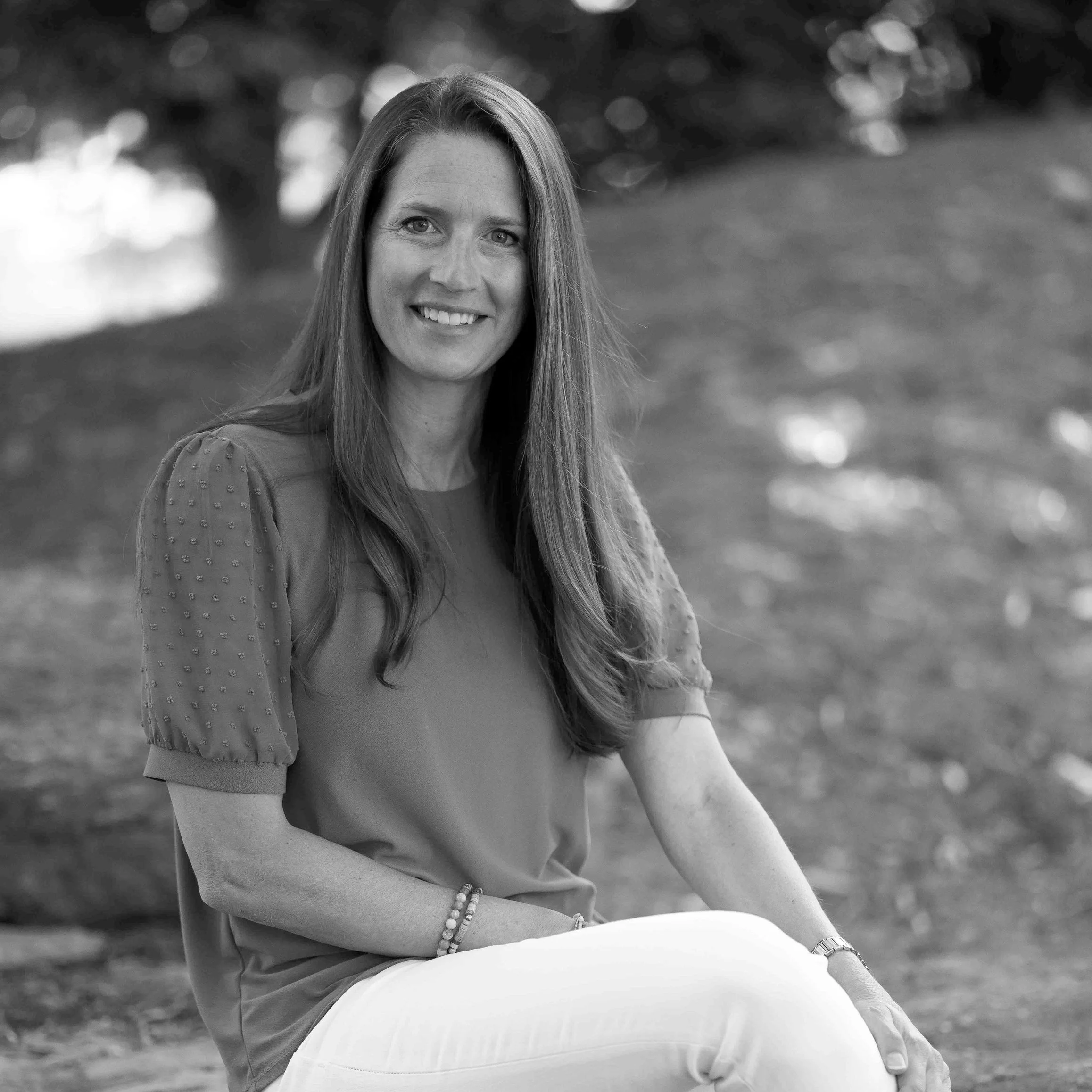 Black and white portrait of Julie Breckenfelder with long hair, sitting outdoors.