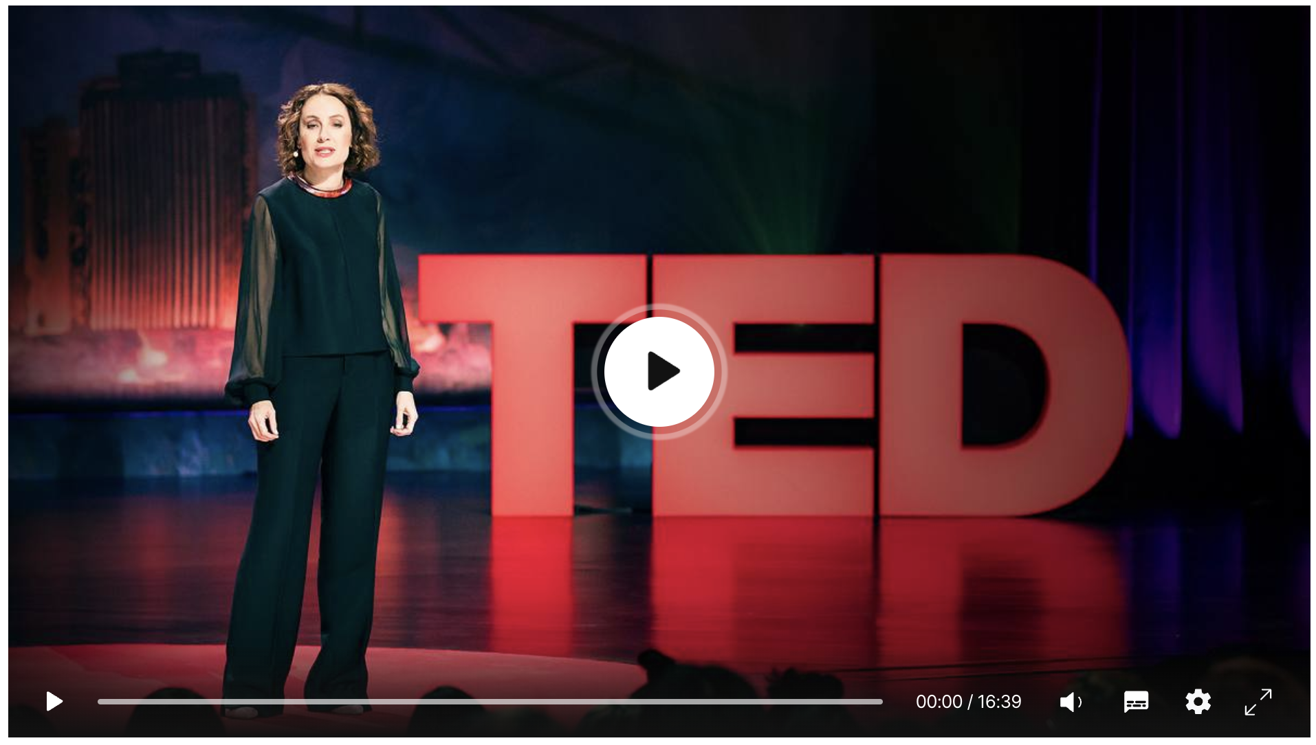 A person standing on a TED Talk stage with the large red TED letters in the background.