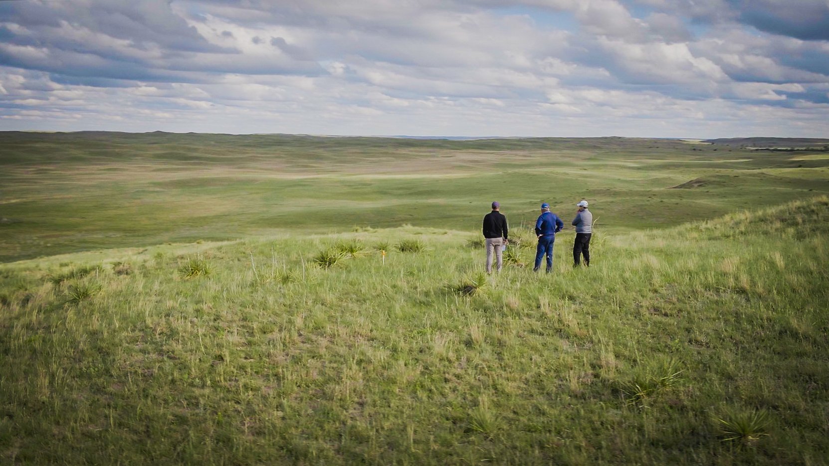 Three golfers standing on a vast plain.
