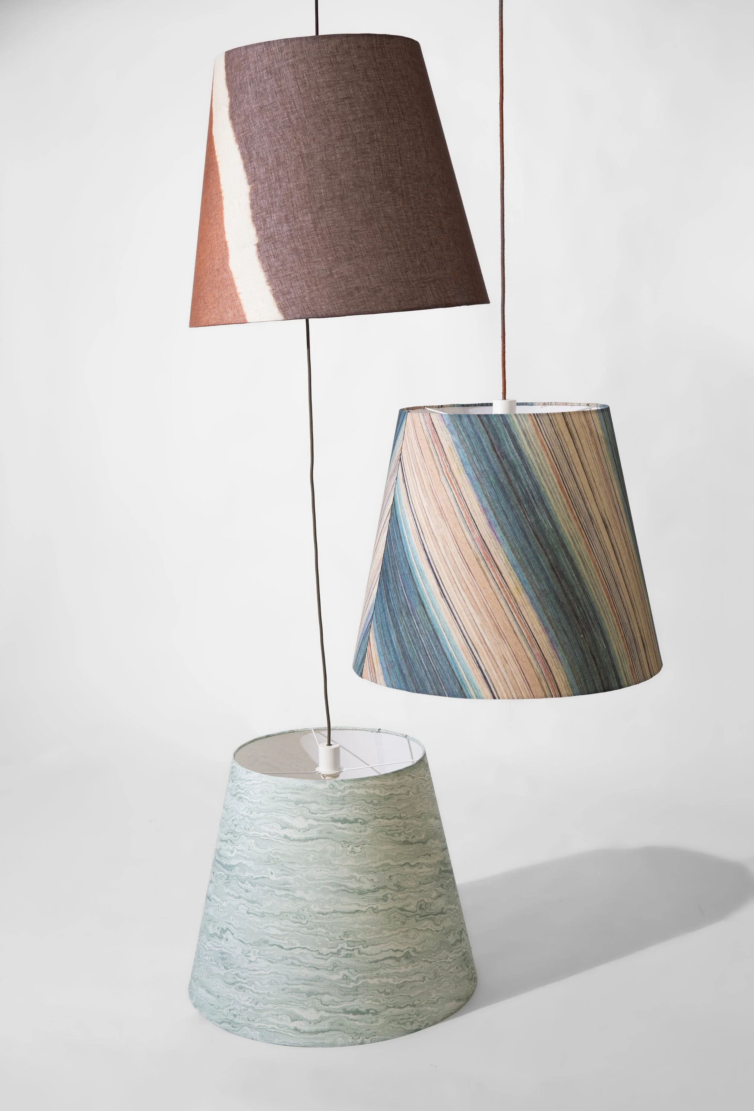 Tre paralumi sospesi di diversi stili e colori su sfondo bianco.