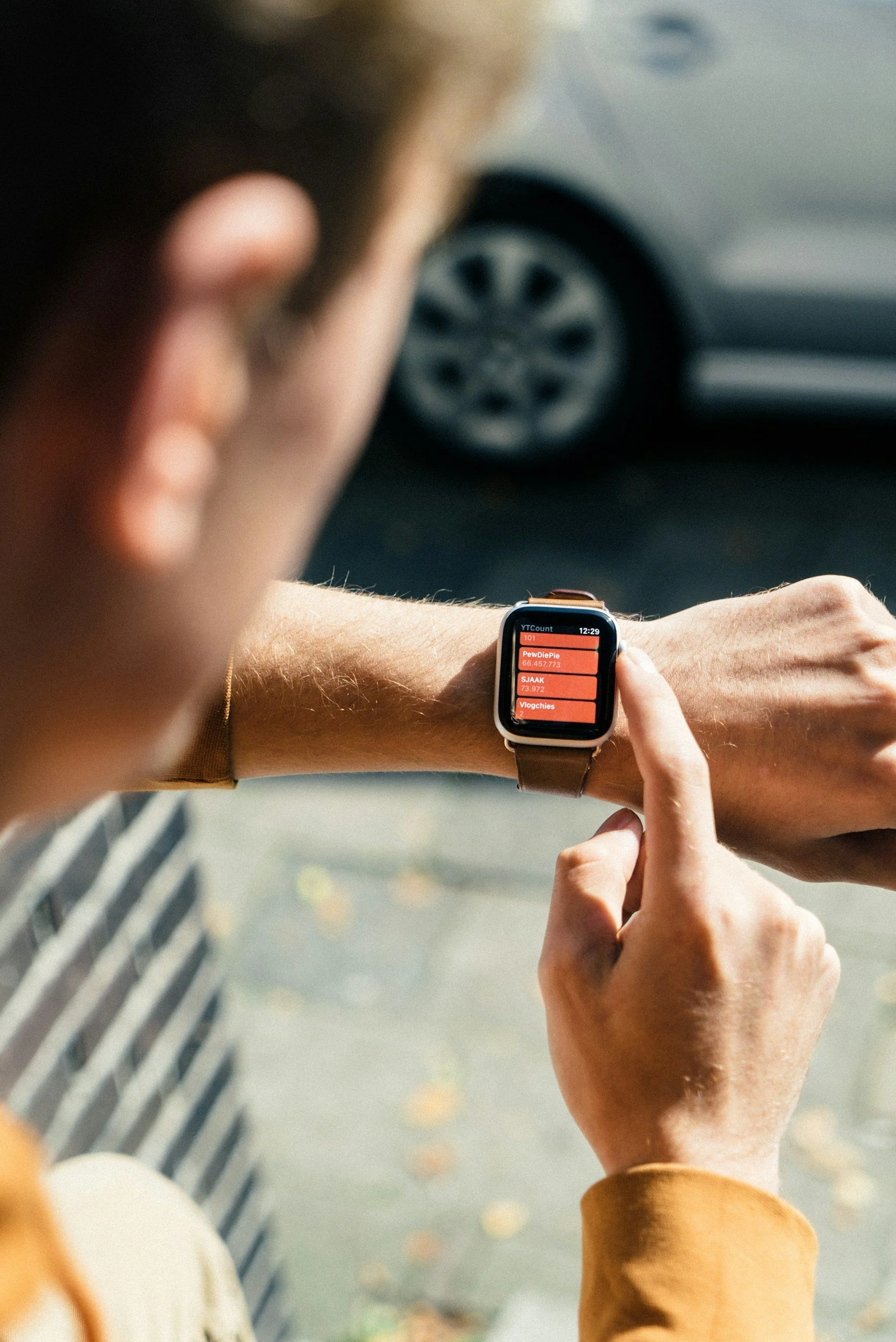 A person looking at a smartwatch on their wrist, with a car parked in the background.