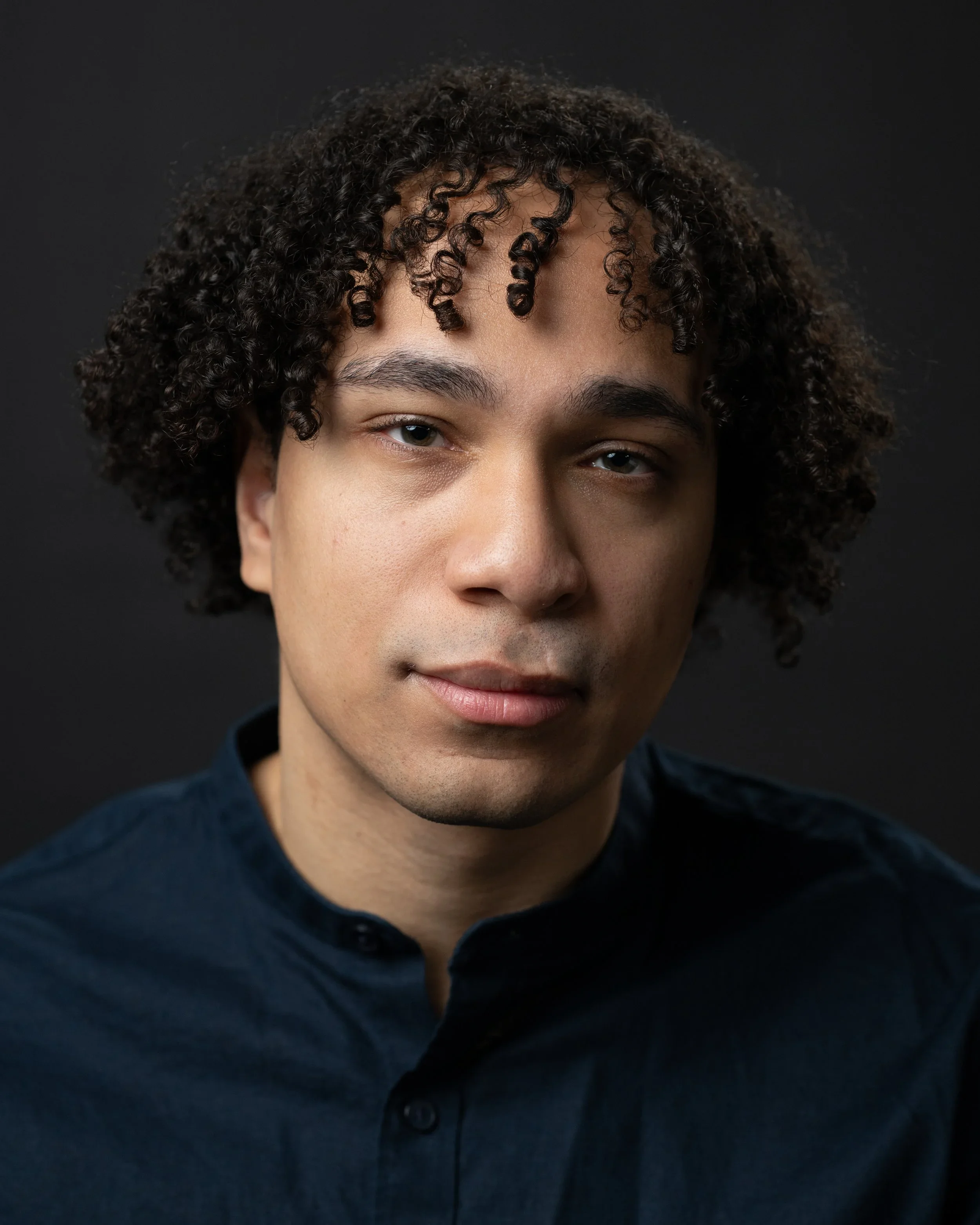 Close-up portrait of a Ellis Finney wearing a dark blue button-up shirt, against a black background.