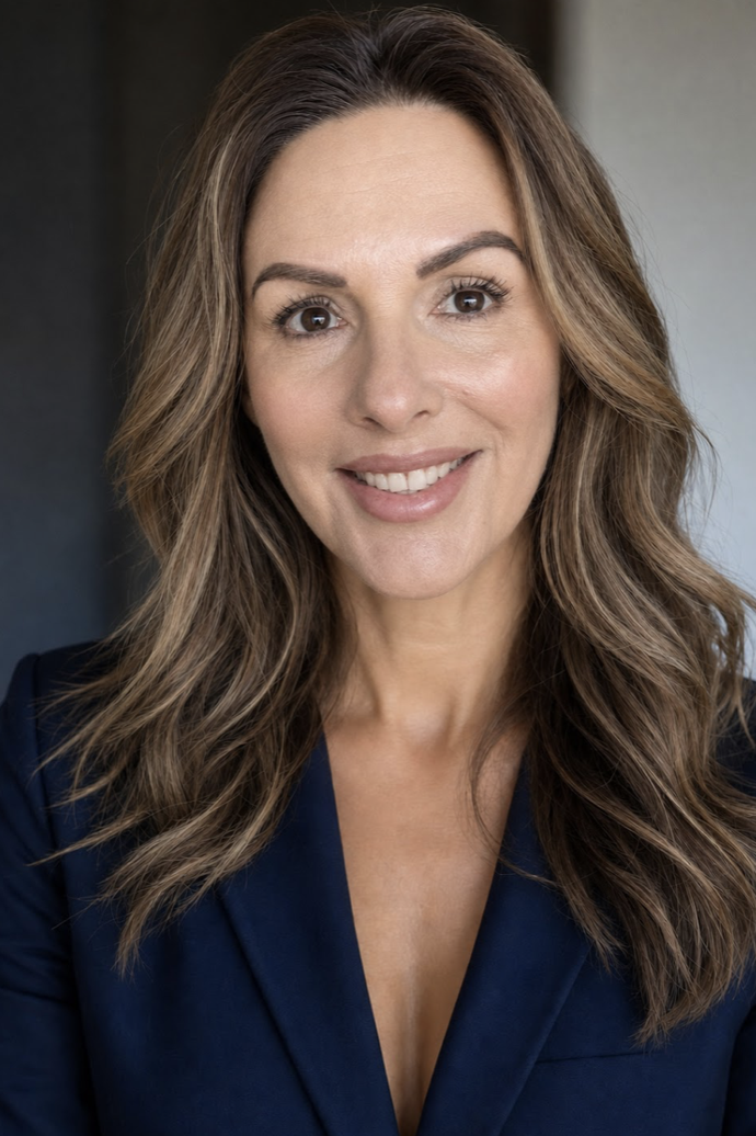 A woman with long wavy brown hair, wearing a dark blue blazer, smiling at the camera.