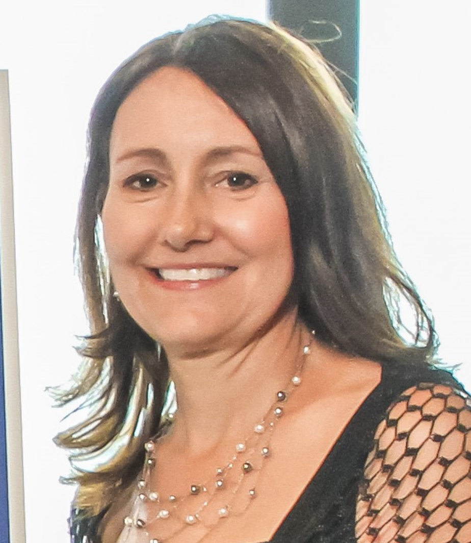 A smiling woman with shoulder-length brown hair, wearing pearl necklaces and a black mesh top.