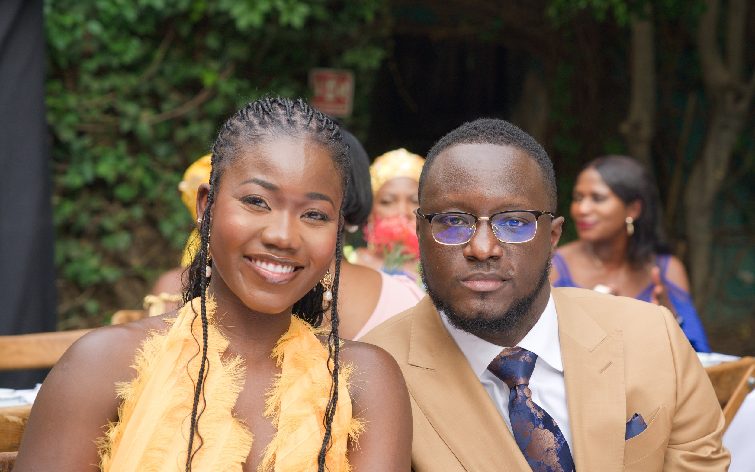 A smiling woman and a serious man at an outdoor formal event.