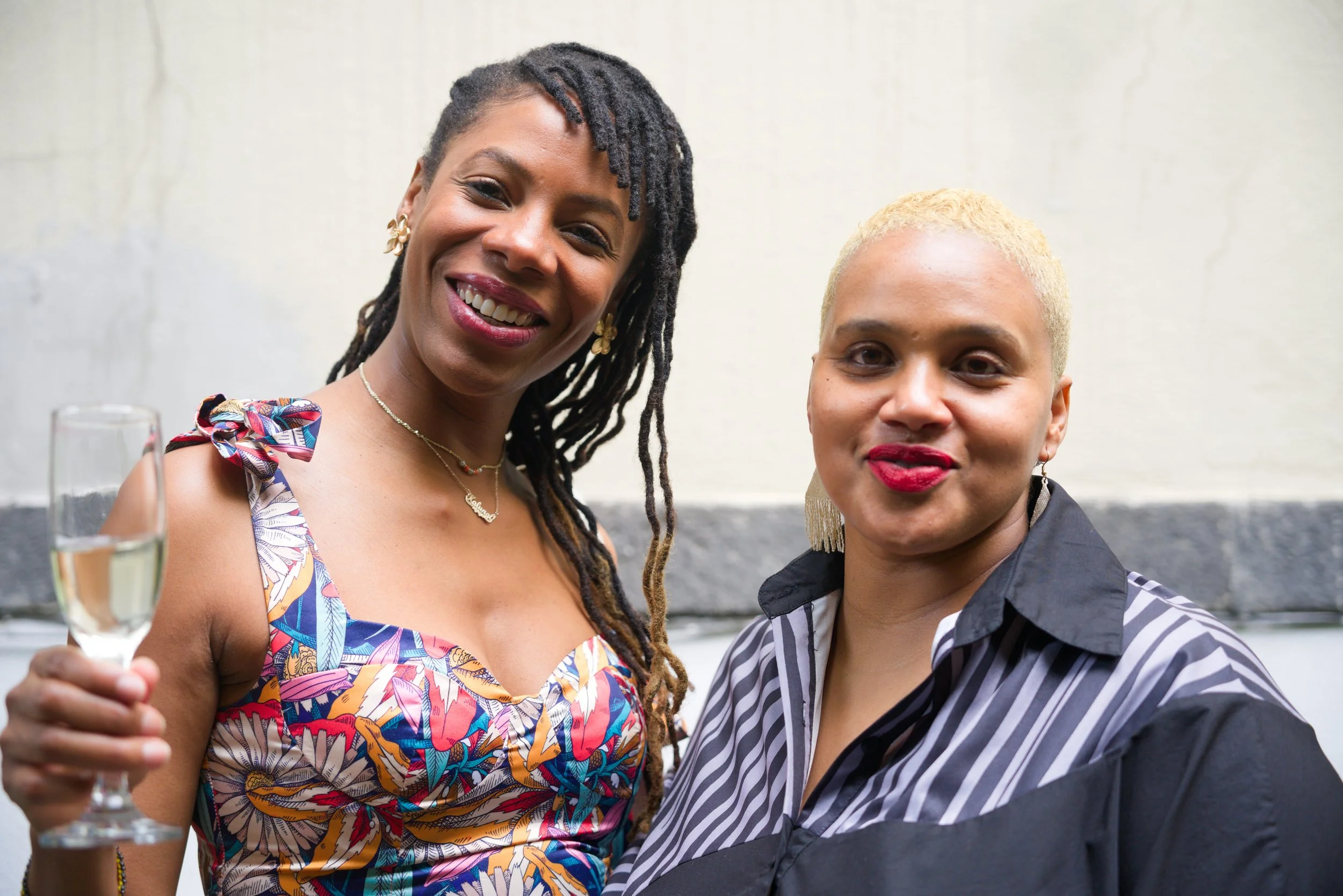 Two women smiling and posing together at a social event; one holding a glass of champagne.