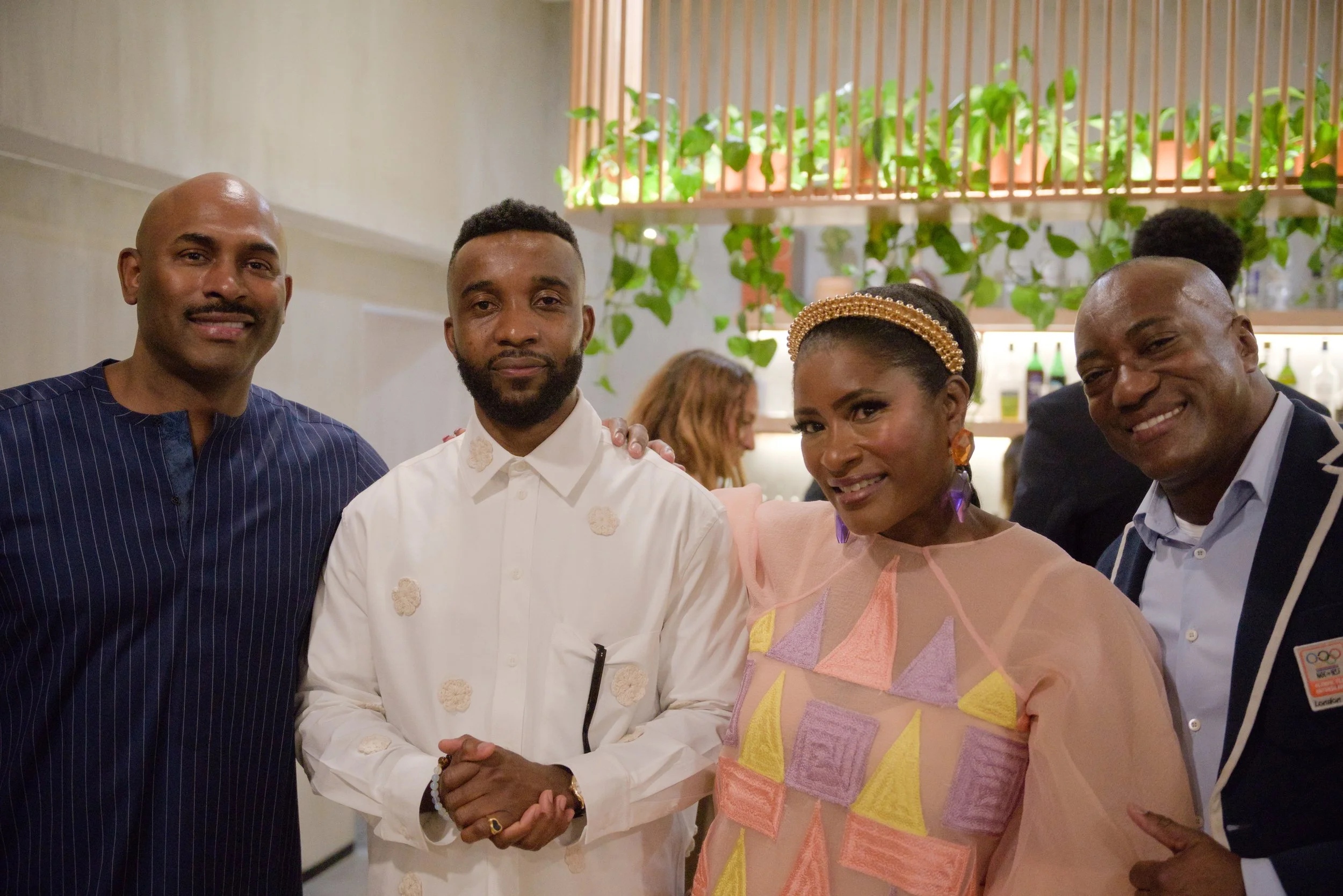 Four people posing together at an indoor event, with a woman in colorful attire and a man in formal dress among them.