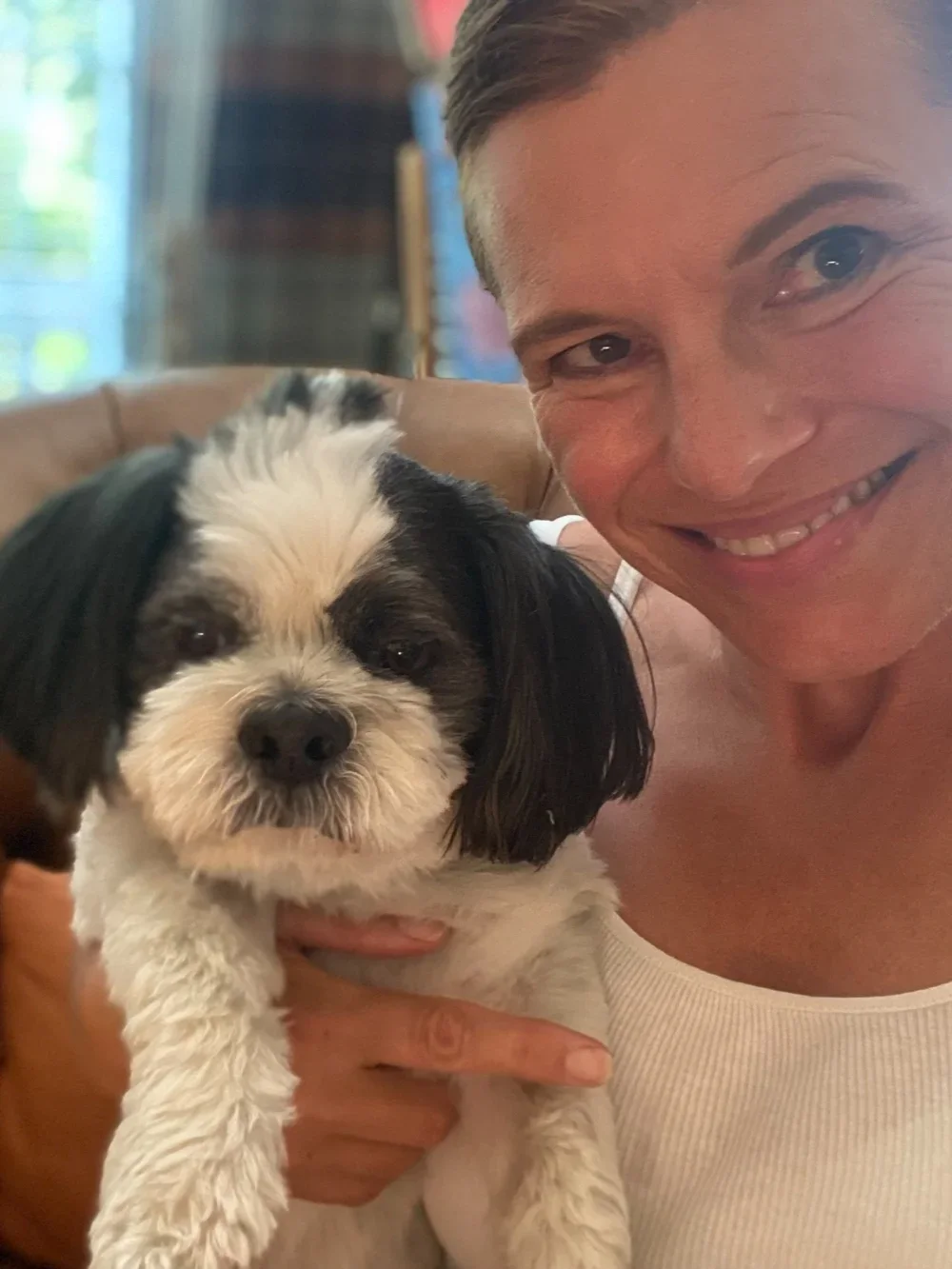 A smiling woman holding a small black and white dog indoors.