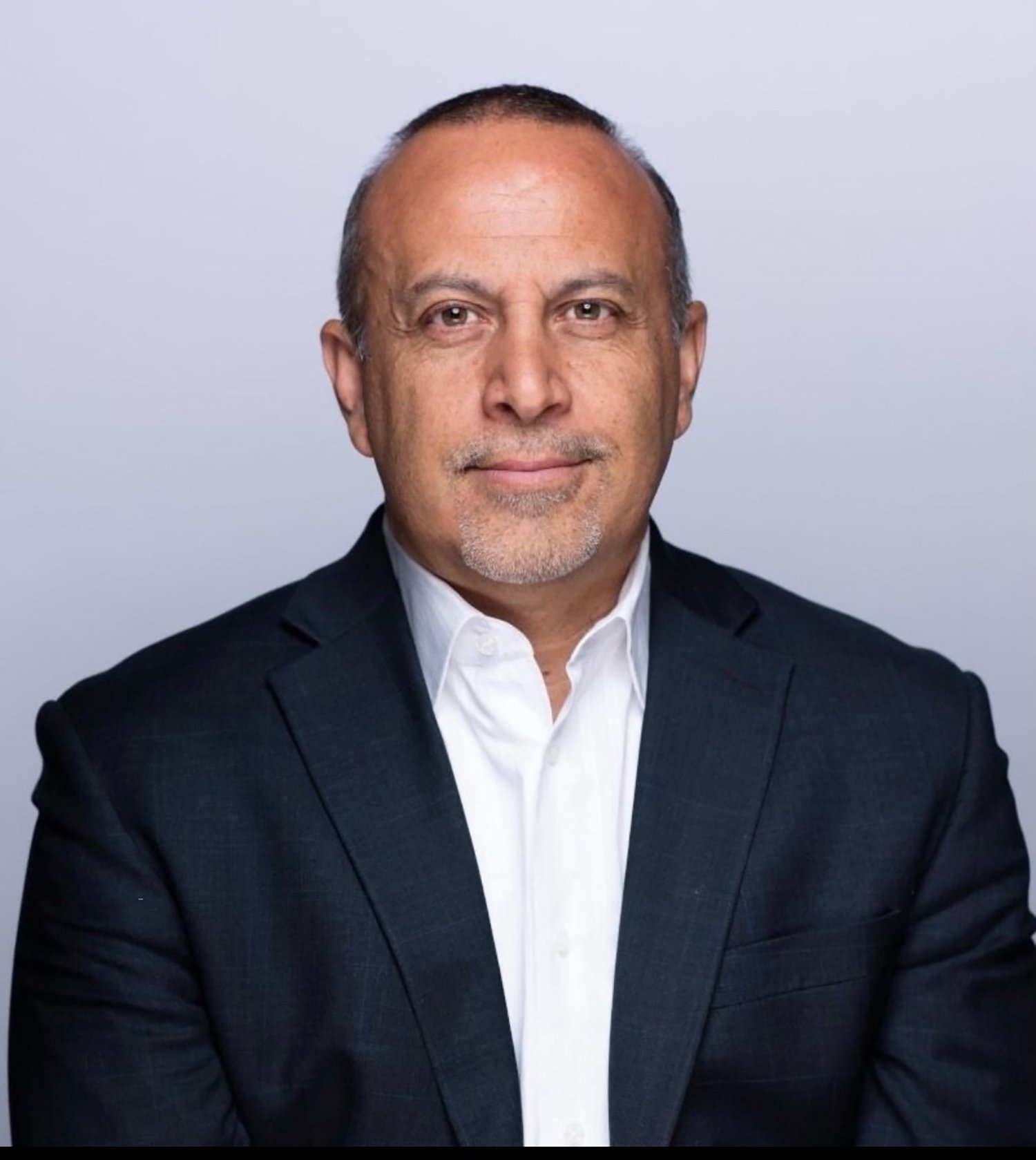 Headshot of a man in a dark suit and white shirt, posing against a light background.