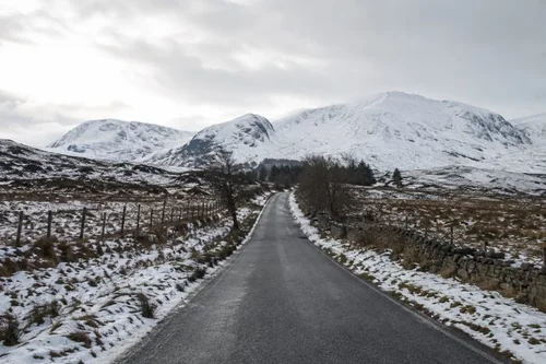Winter road through British countryside with snowy mountains in the distance