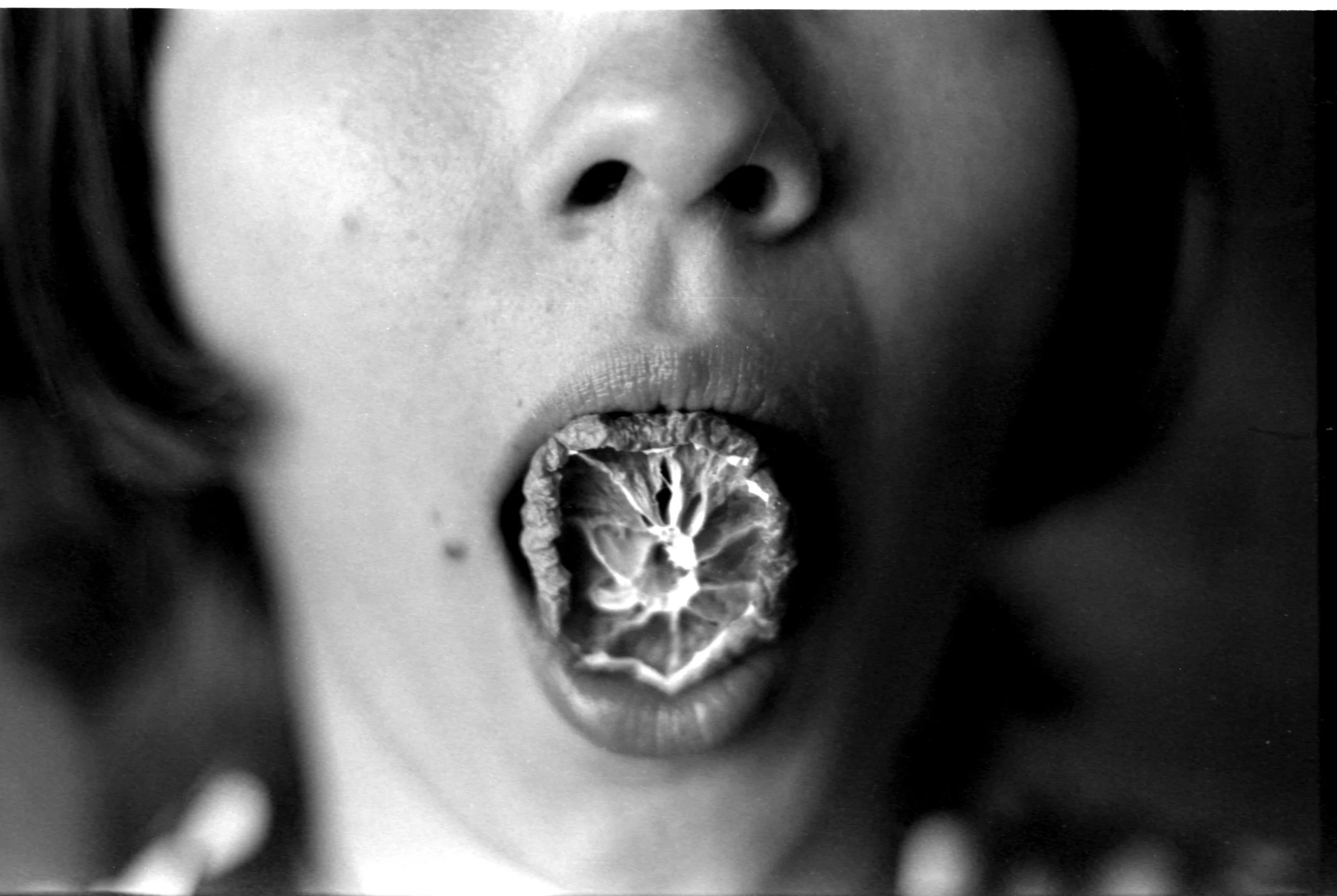 Black and white 35mm self portrait of myself with a dried orange in my mouth. Uncanny and strange creative photography. 