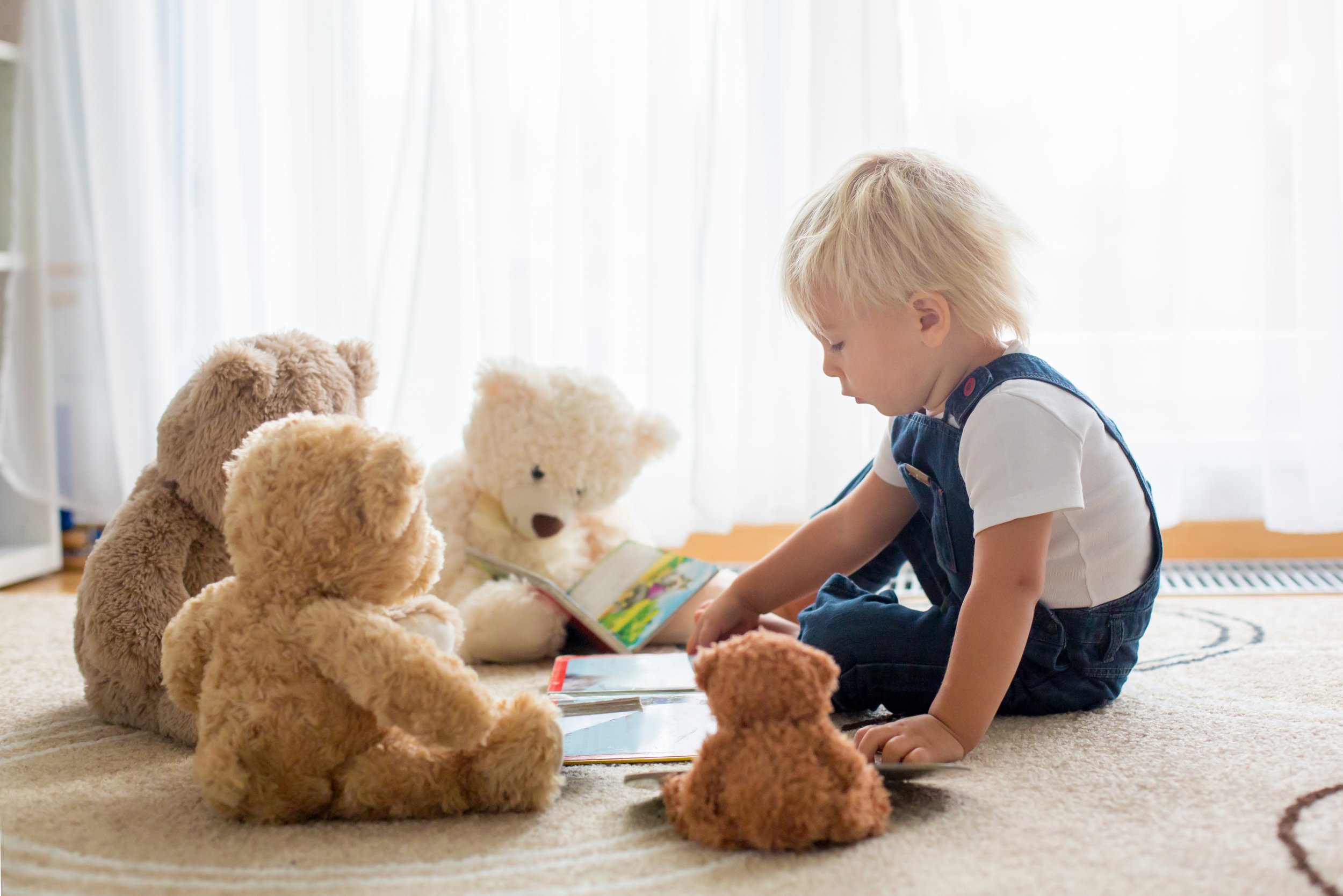 A toddler reading his book to his stuffed animals