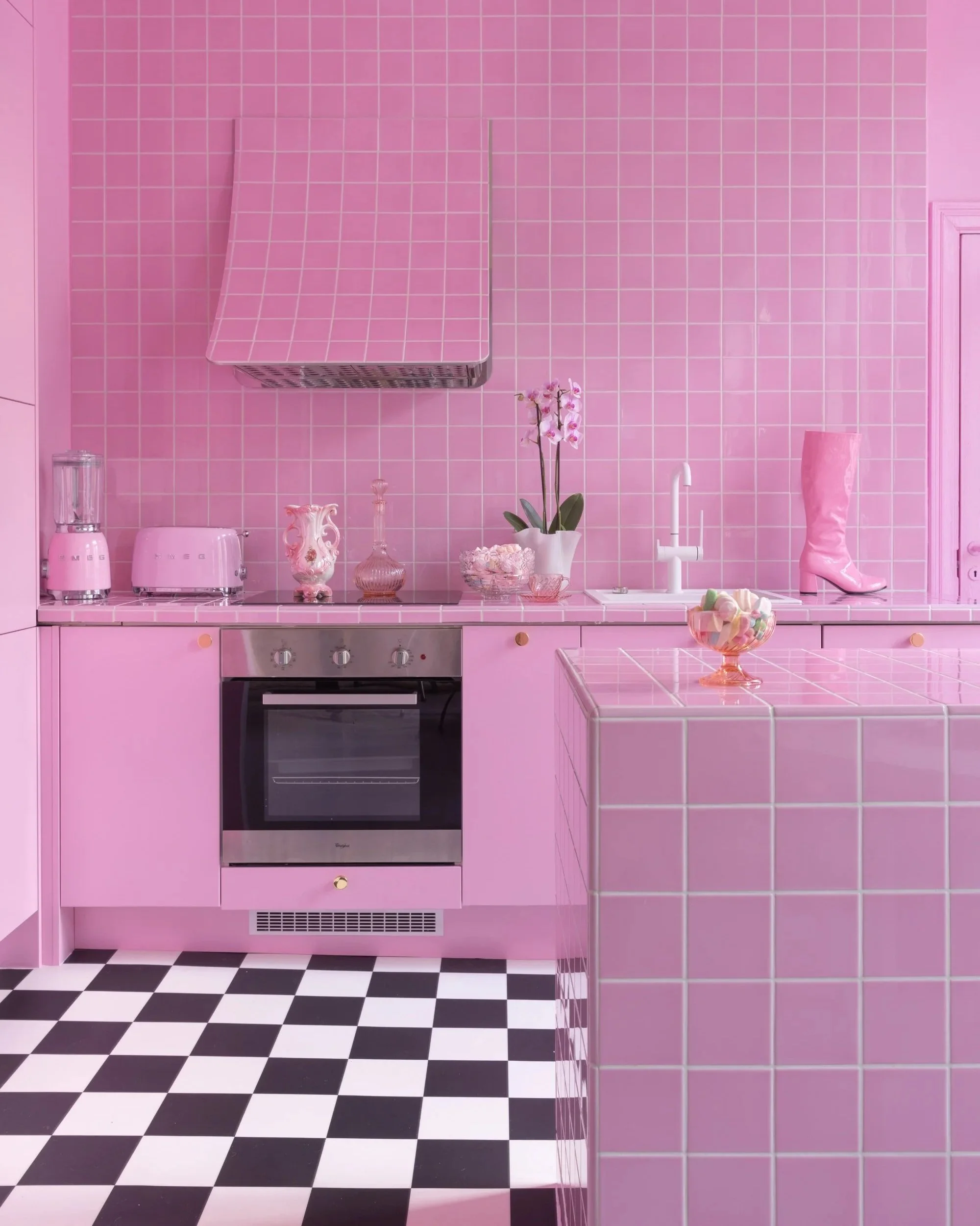Pink tiled kitchen in Janita Autio’s Helsinki home, interior design and styling by Peeta Peltola, featuring checkerboard flooring and a playful, retro-inspired aesthetic.
