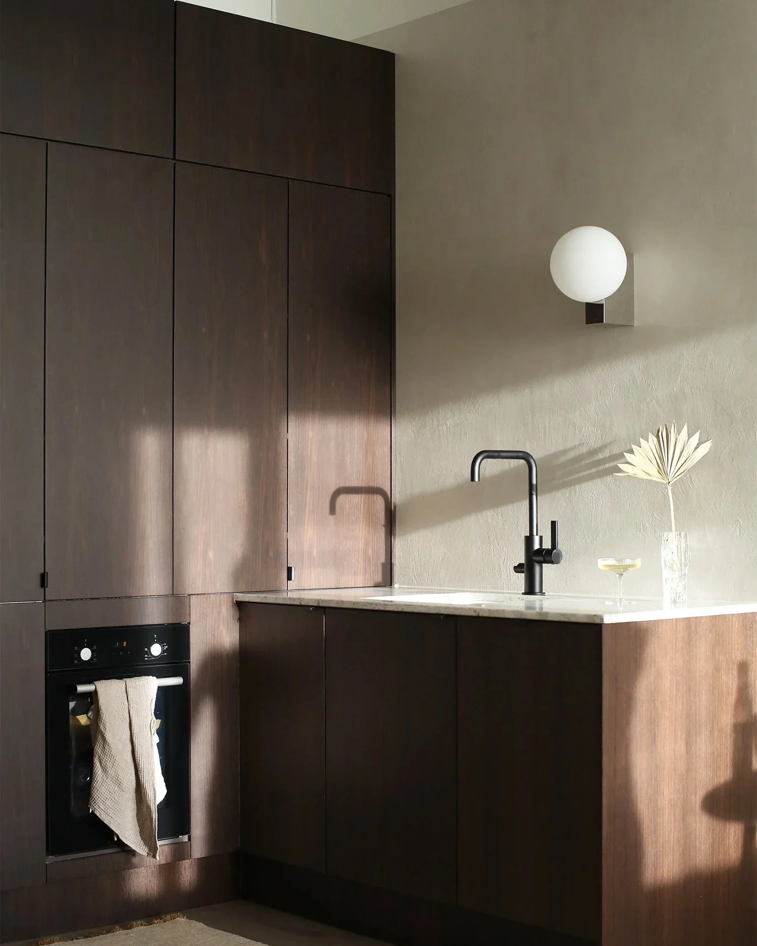 Modern kitchen interior in a renovated 1930s Helsinki apartment, interior design by Peeta Peltola, featuring dark wood cabinetry, natural materials and a refined, minimal aesthetic.