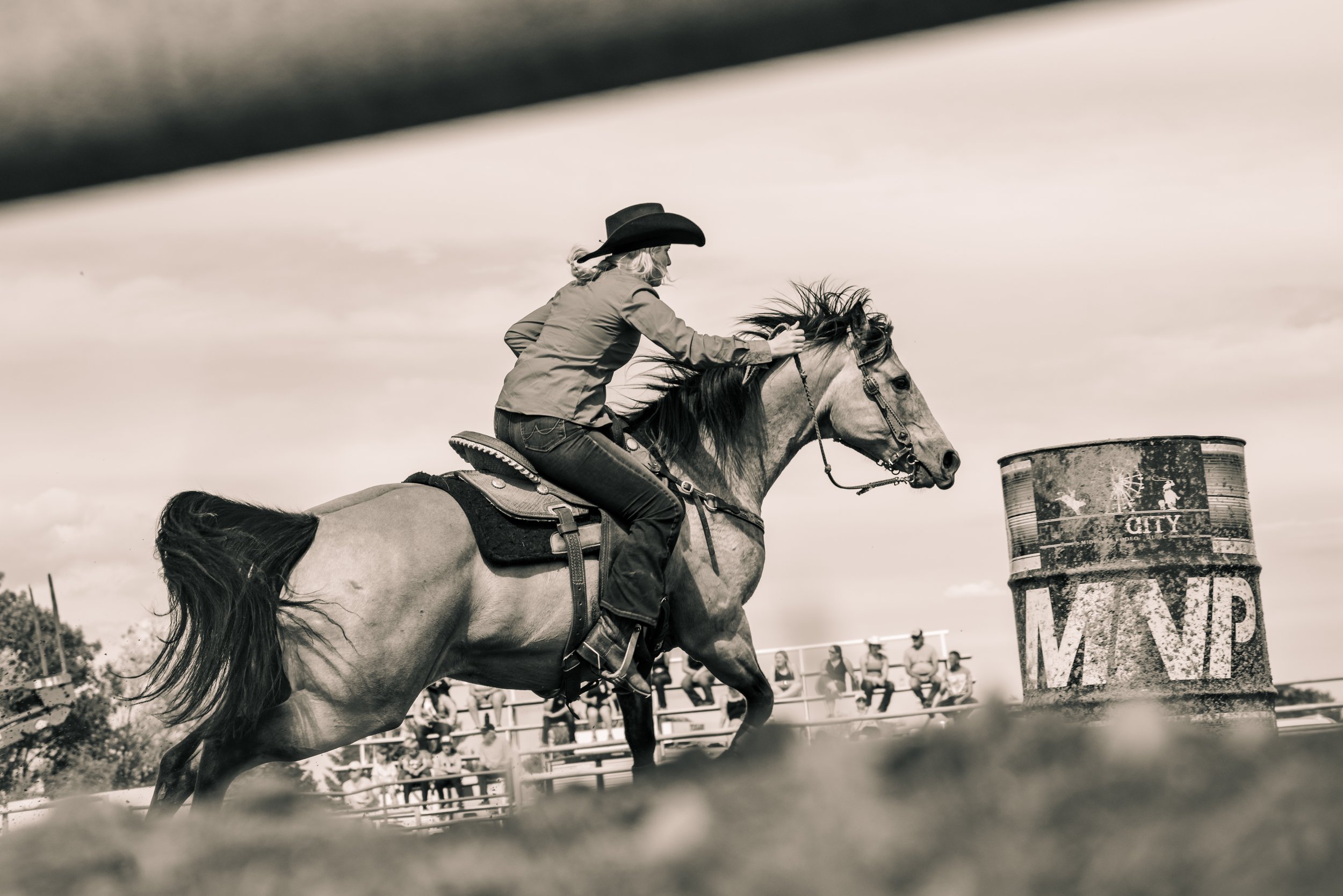 Cowgirl on horseback barrel racing in a rodeo arena with spectators in the background.