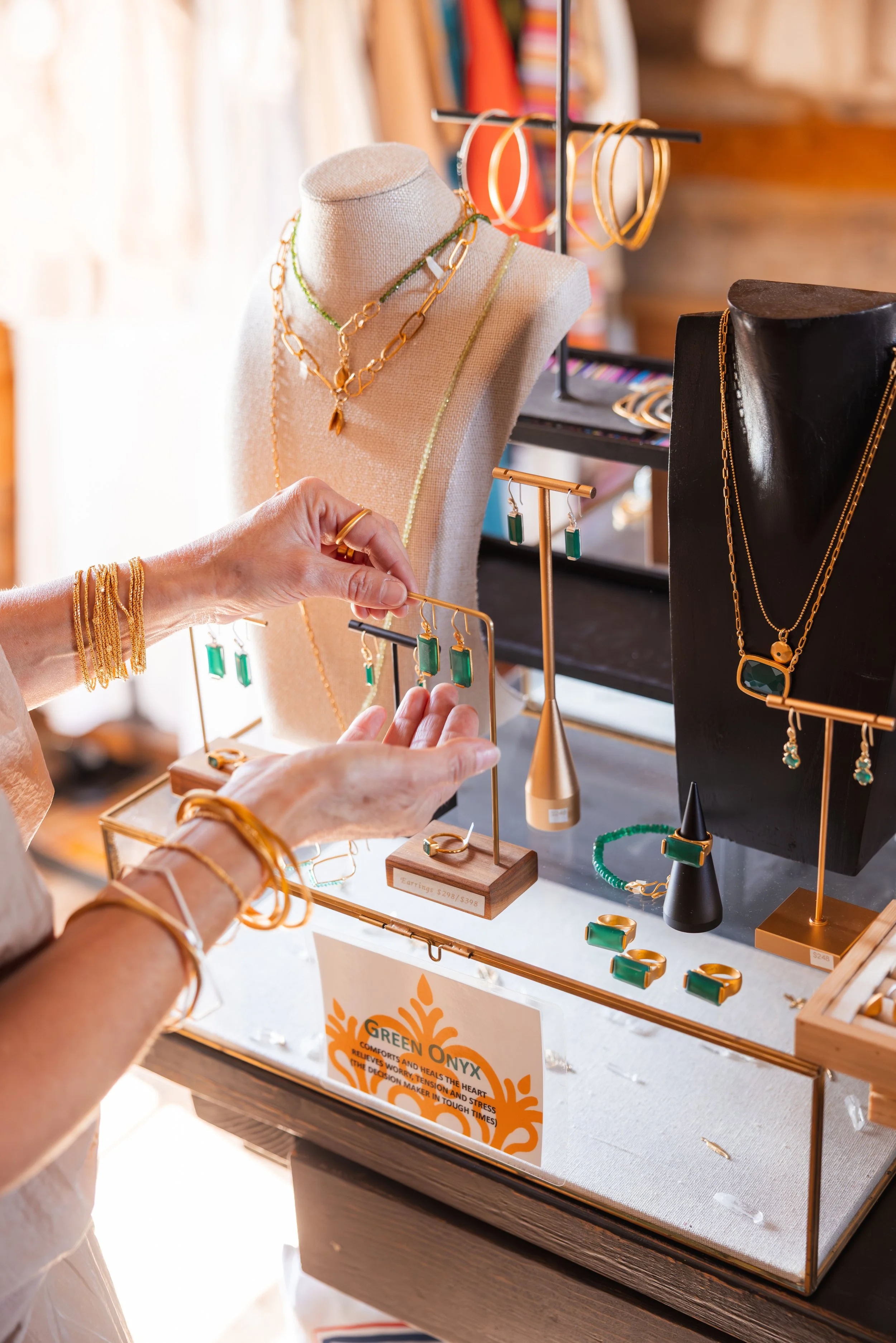 Person shopping for jewelry at Via Vandi with various gold and green onyx jewelry, including necklaces and earrings, displayed on stands and busts.